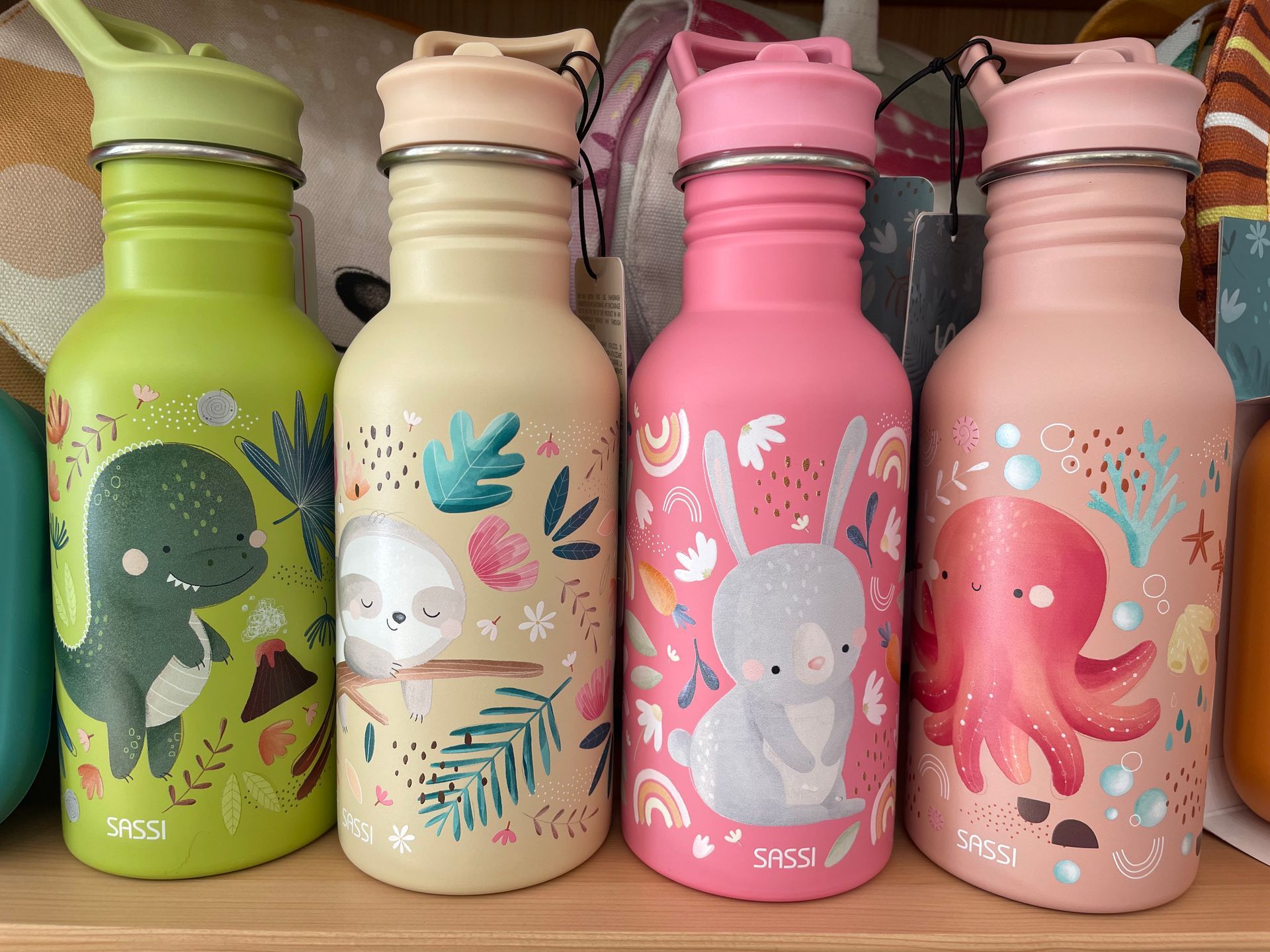 Quattro borracce riutilizzabili dai colori pastello, decorate con polpi colorati e creature marine, disposte in fila su un tavolo