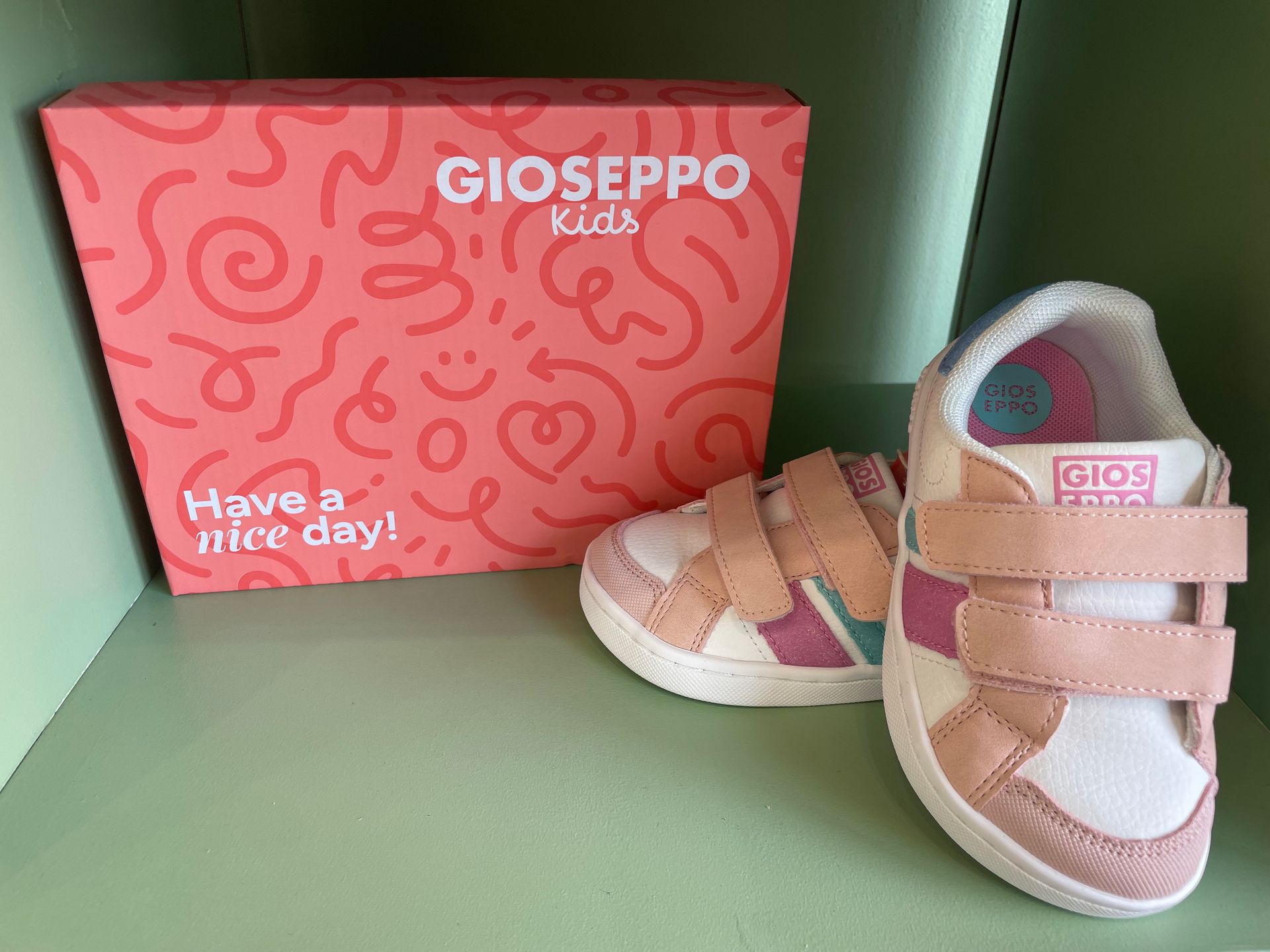 Scarpe rosa da bambina accanto a una scatola di scarpe GIOSEPPO Kids color corallo, su una superficie verde