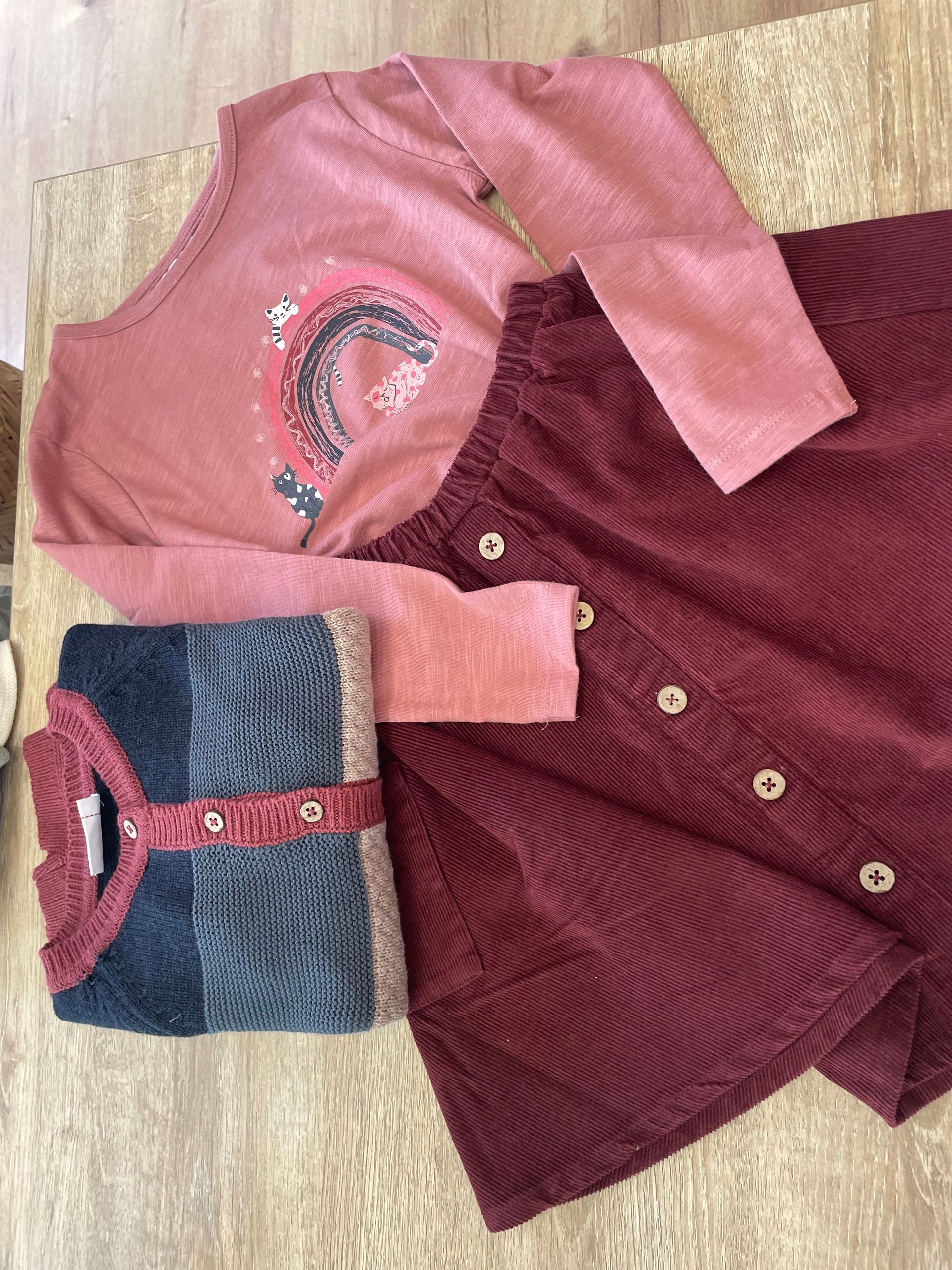 Top ricamato rosa e bordeaux con un capo blu fantasia ripiegato su un pavimento di legno