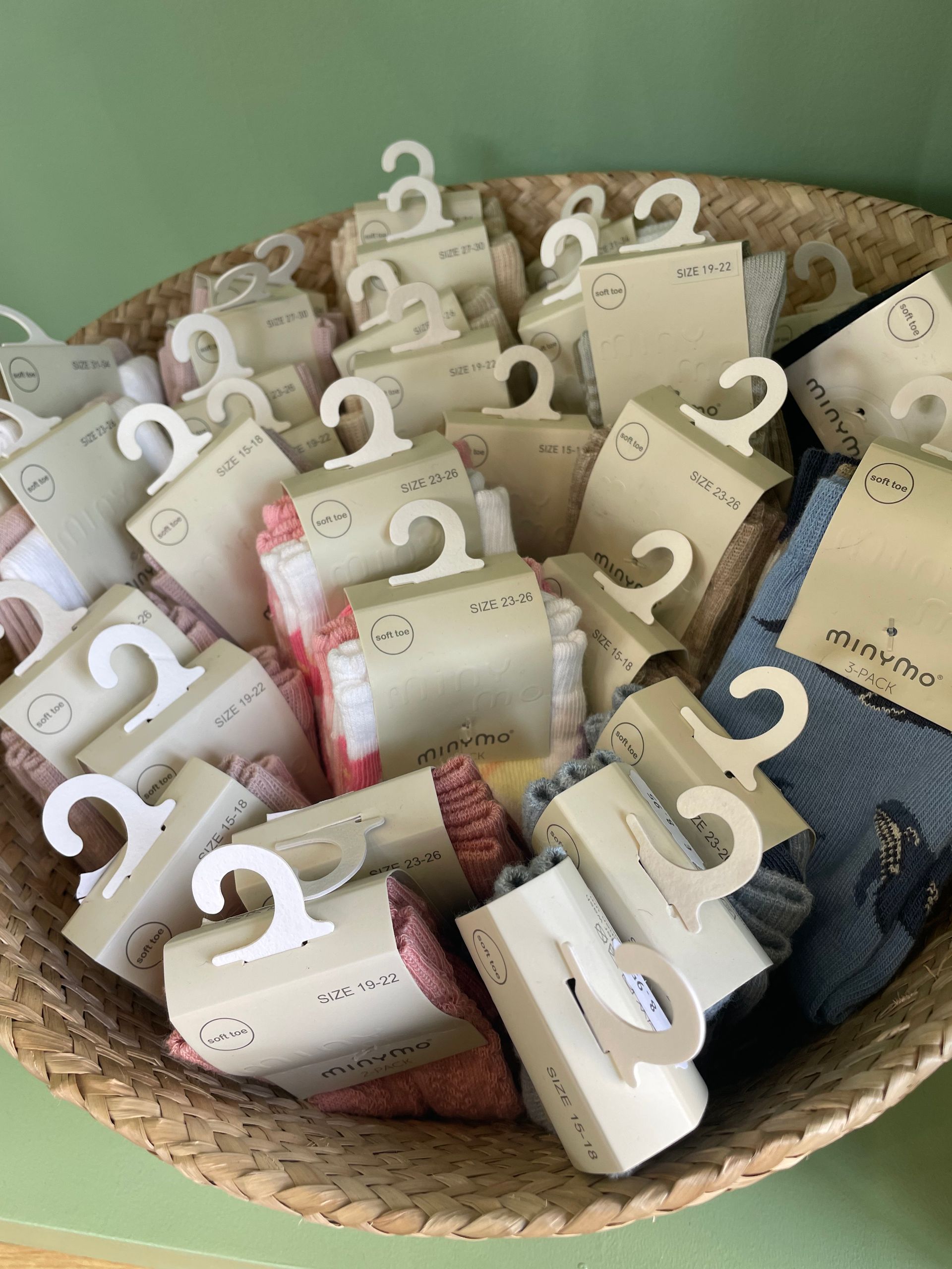 Cesto di sacchetti regalo assortiti color crema e marrone scuro, con manici bianchi, su sfondo verde