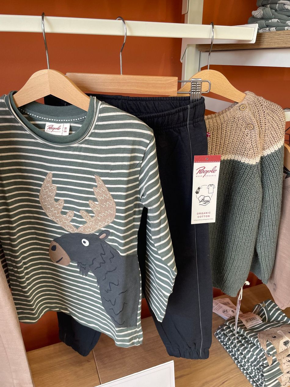 Camicia a maniche lunghe a righe con grafica di un alce, appesa a una gruccia nell’esposizione di un negozio di abbigliamento