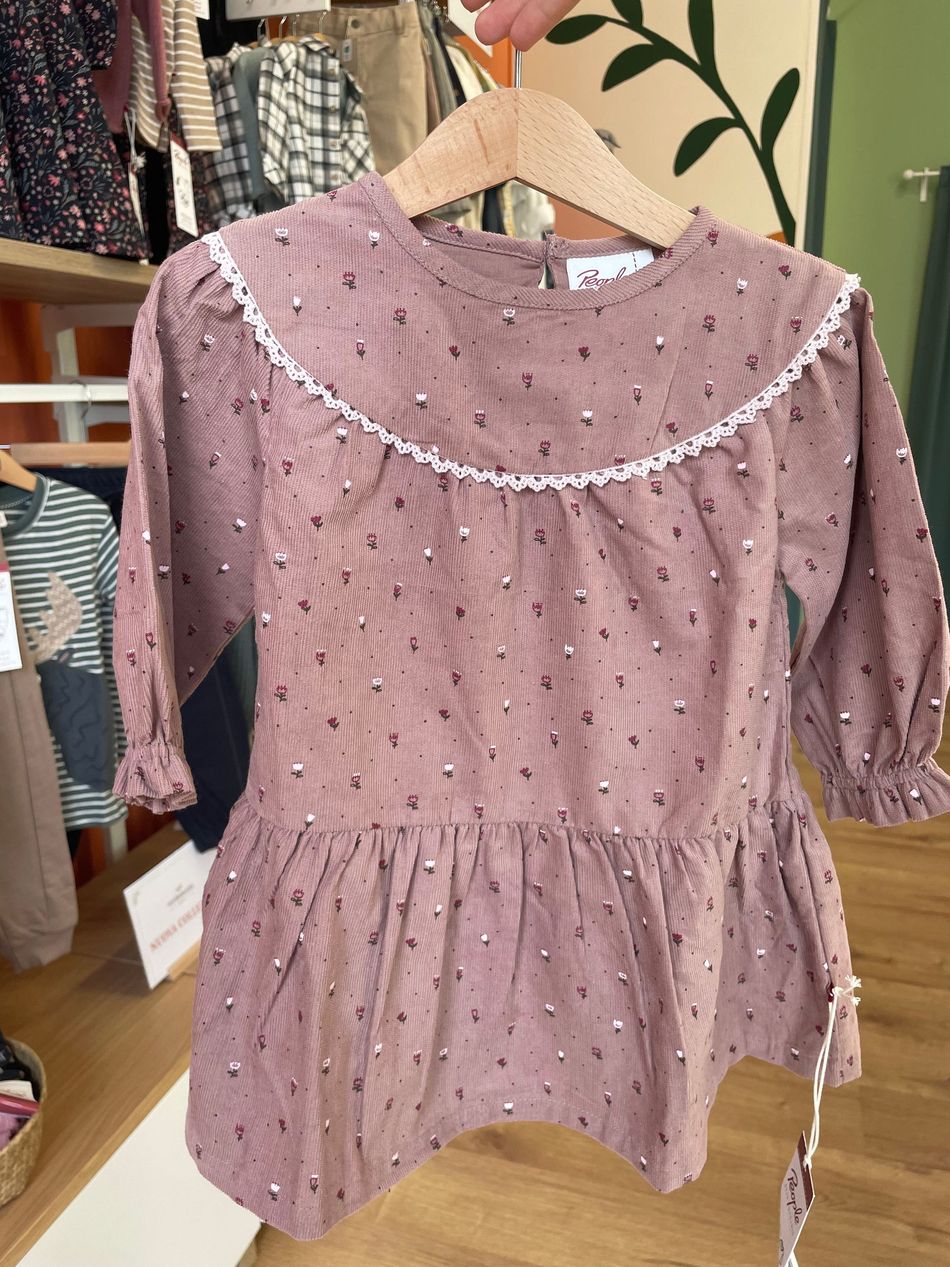 Abito rosa fantasia con bordi smerlati bianchi appeso a una gruccia in un negozio di abbigliamento