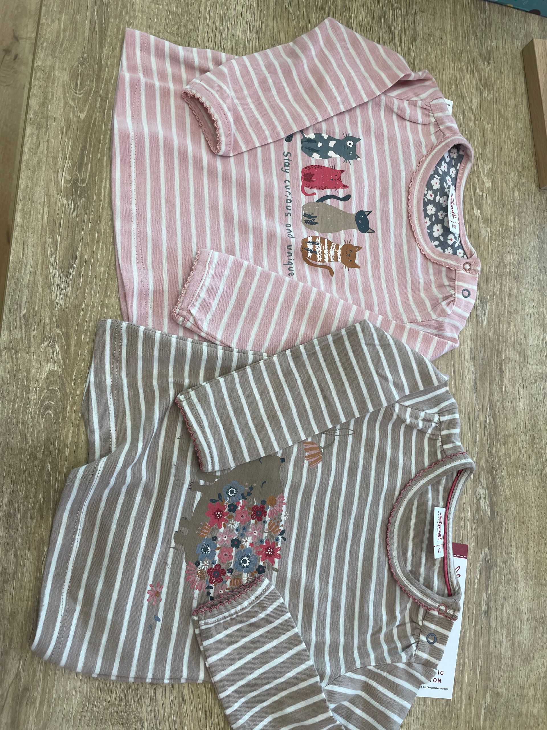 Due maglie a maniche lunghe a righe su una superficie ruvida, una rosa e una grigia, con piccoli motivi sul davanti