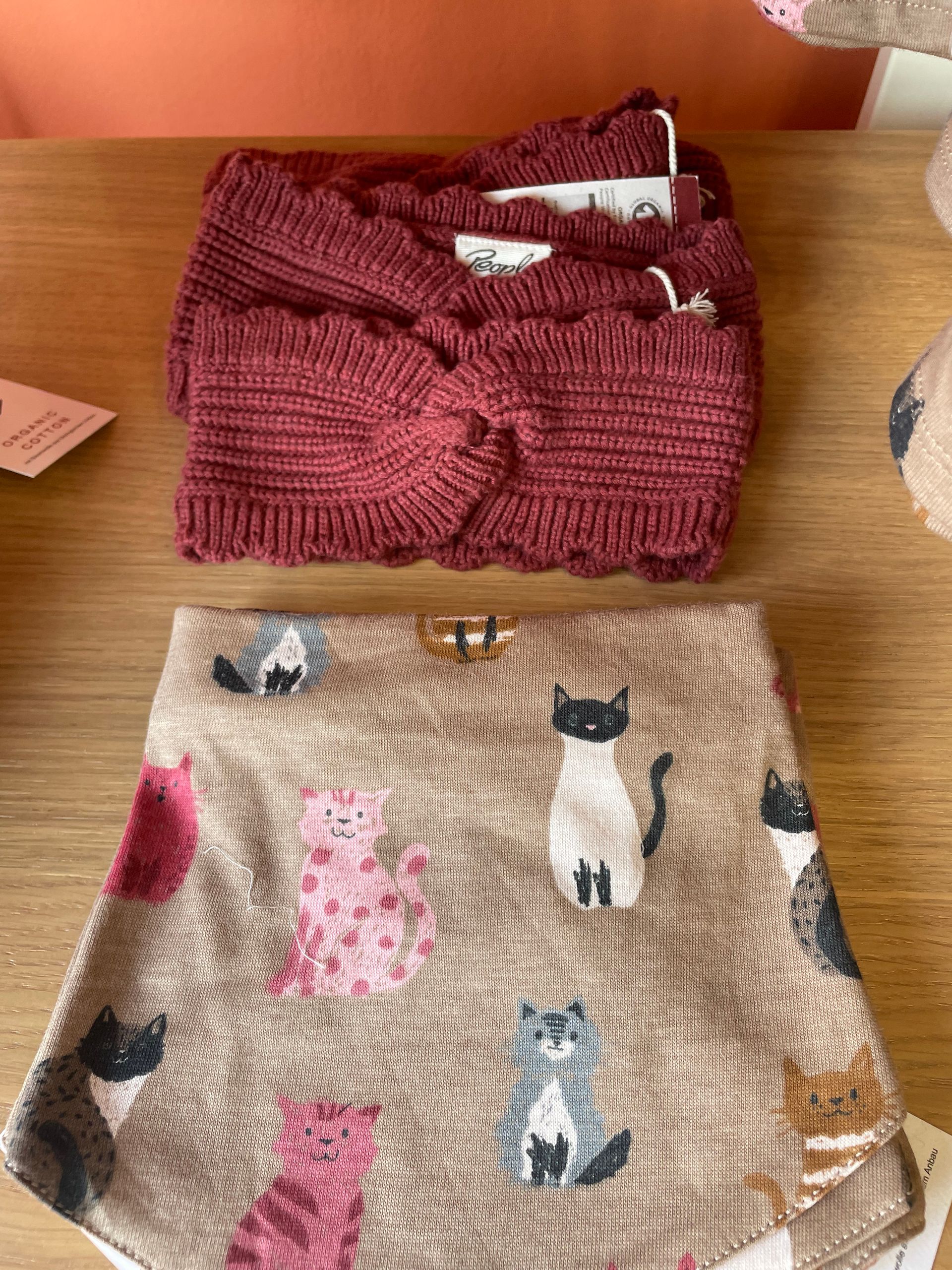 Due capi in maglia piegati su una superficie di legno: un top bordeaux e dei pantaloncini beige con fantasia a gatti.