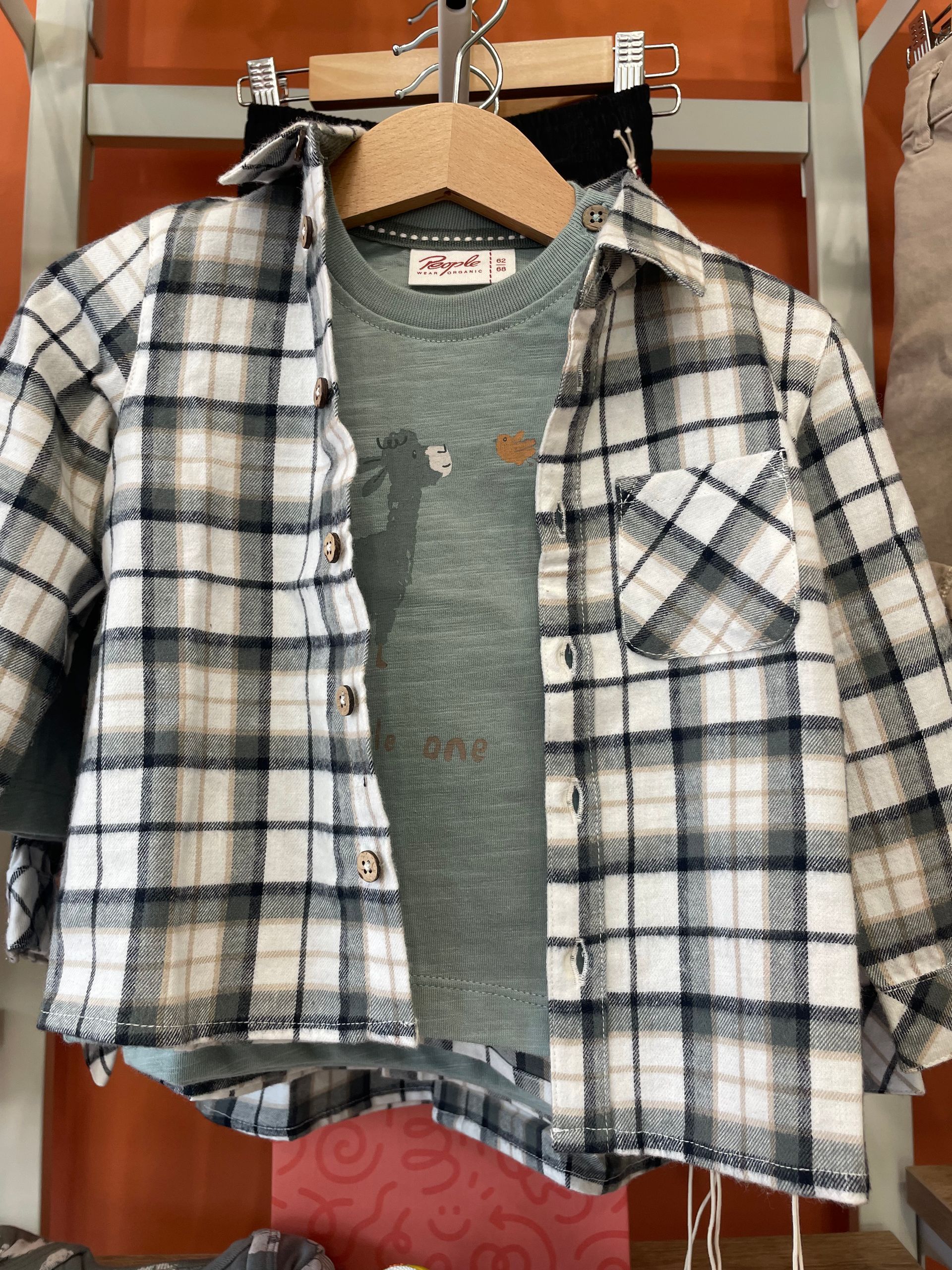 Camicia a quadri bianchi e neri sopra una maglietta verde, appesa davanti a un armadio di legno.