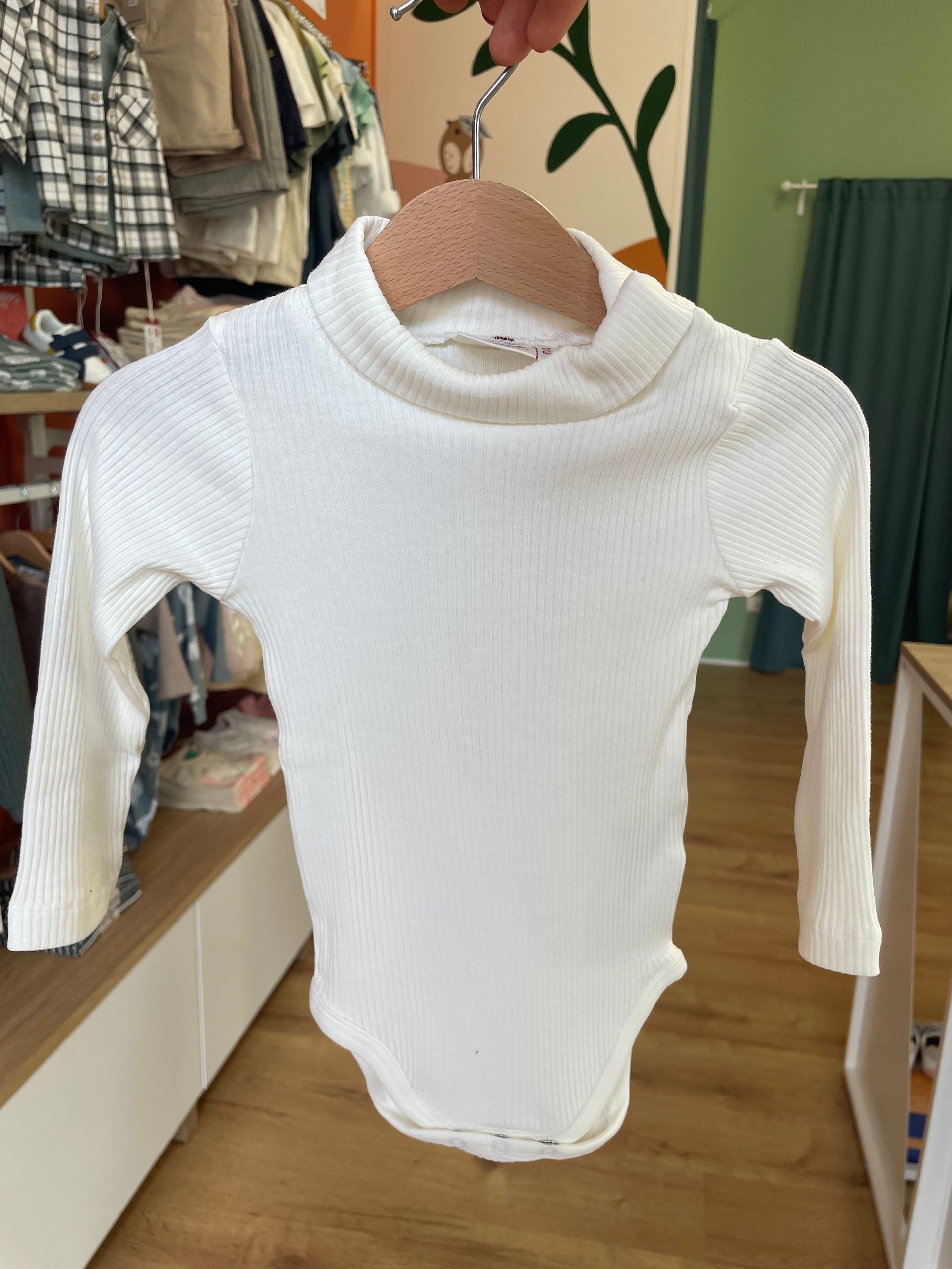Maglia bianca a coste a maniche lunghe con collo alto, appesa a una gruccia in un negozio di abbigliamento