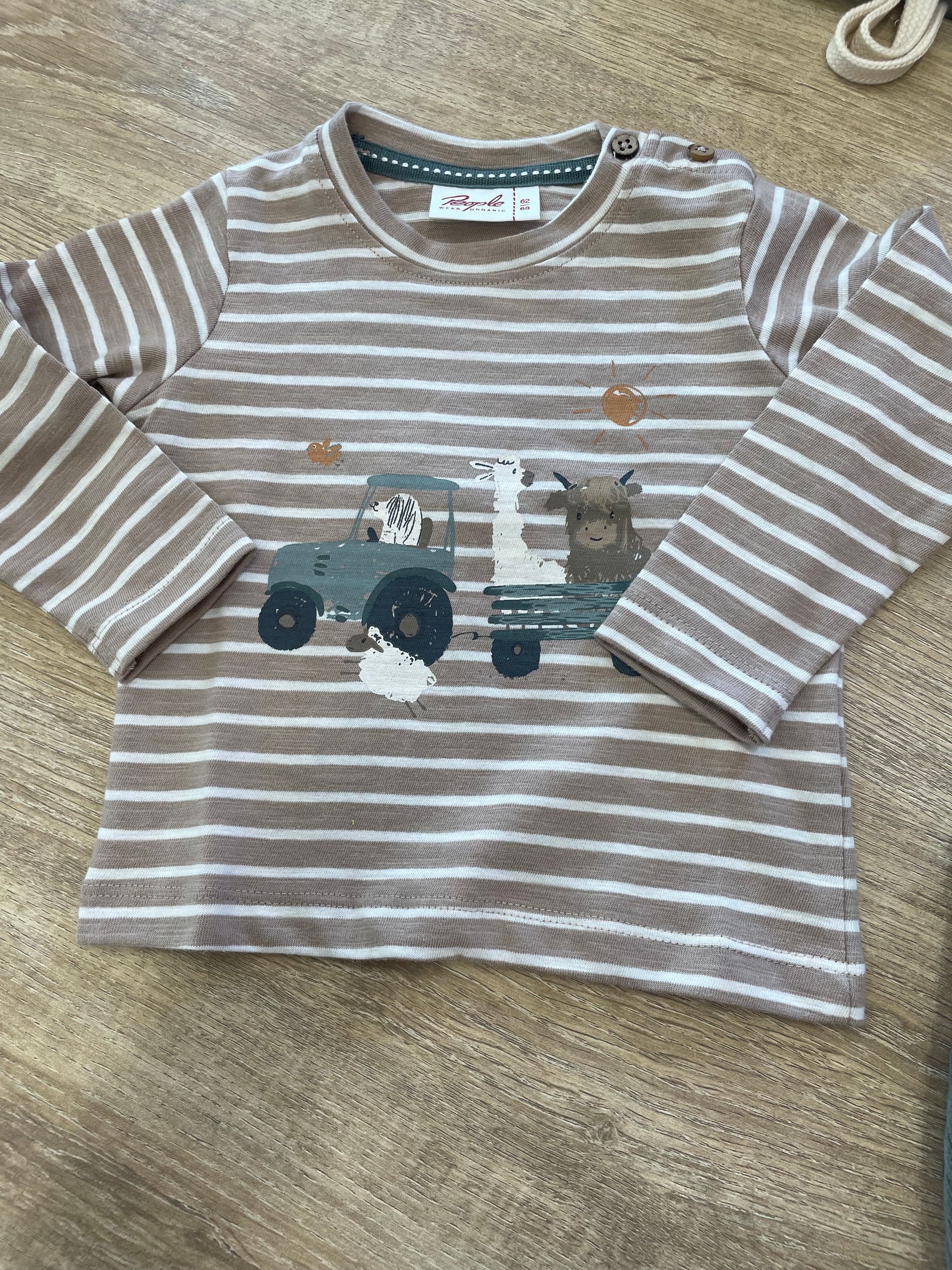 Maglia a maniche lunghe a righe grigie e bianche, con una grafica di un camion sul davanti, appoggiata su un tappeto beige.