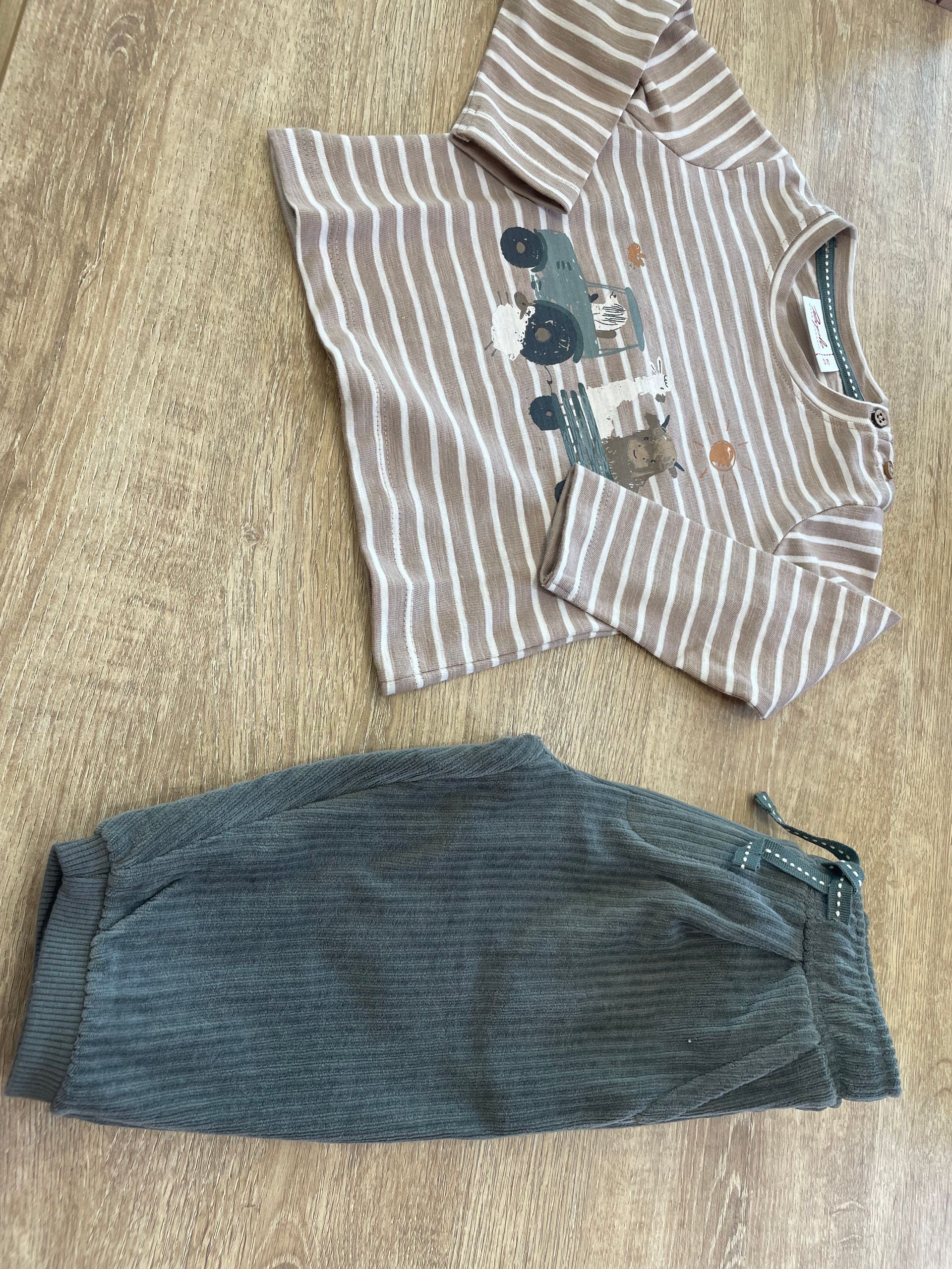 Due vestitini piegati per neonati su un tappeto beige: una tutina a righe a maniche corte e pantaloni blu scuro.