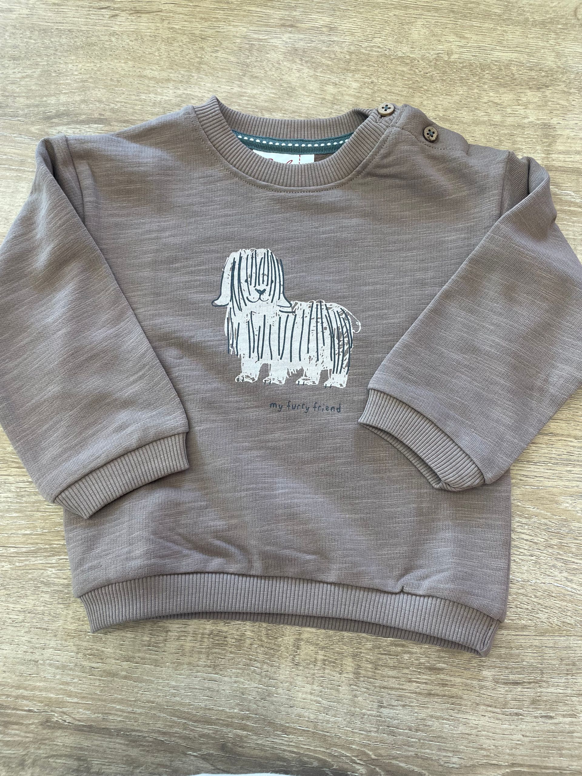 Maglione marrone lavorato a maglia con un coniglietto bianco sul davanti, disteso su una superficie beige