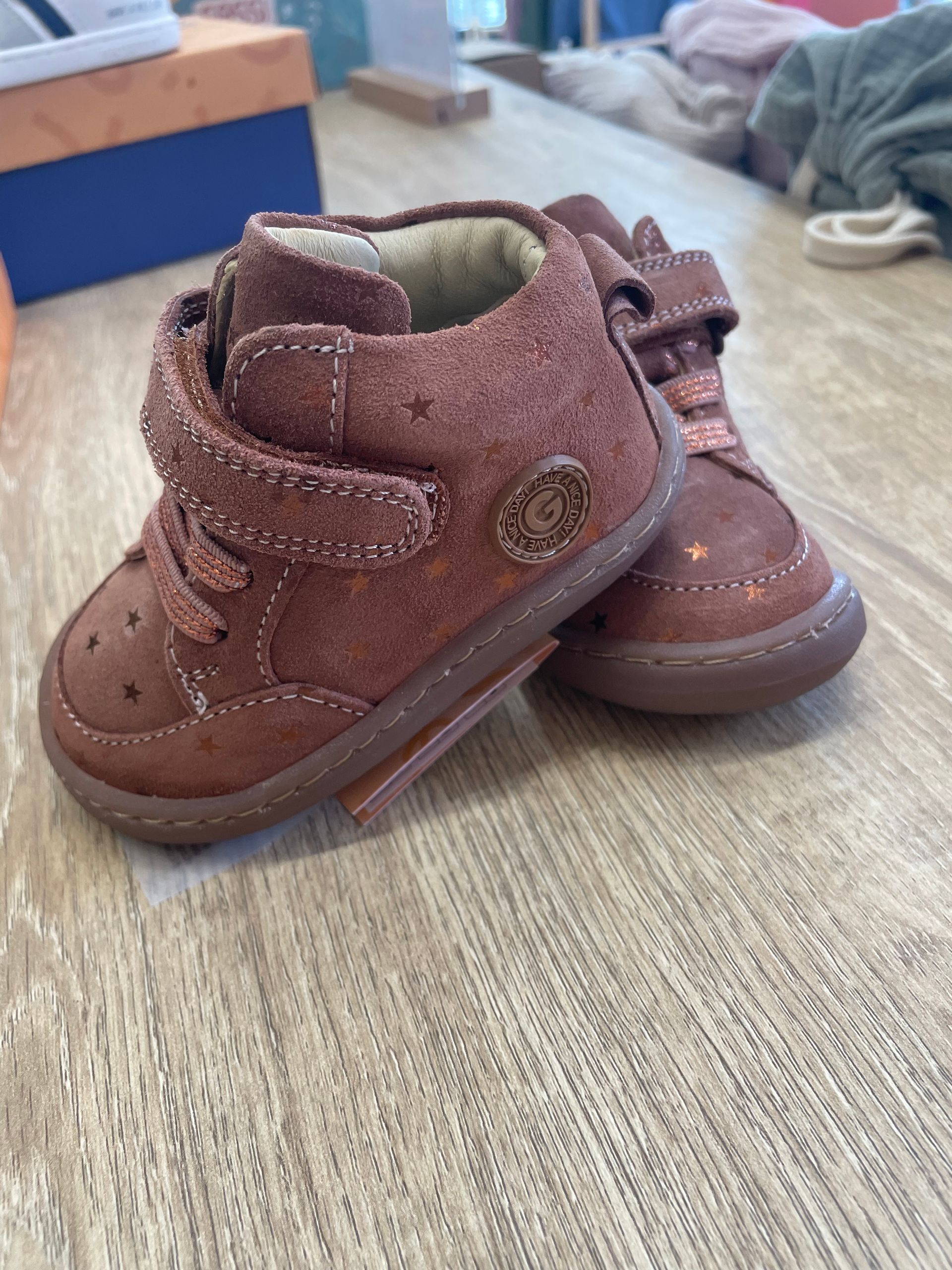Stivaletti marroni per bambini con chiusure in velcro, su un pavimento ricoperto di moquette