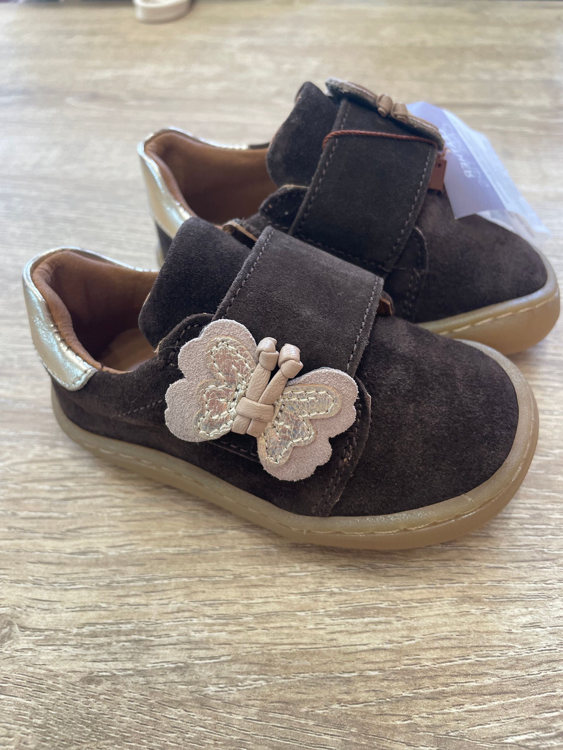 Scarpe marroni da bimbo con cinturini floreali su una superficie di legno
