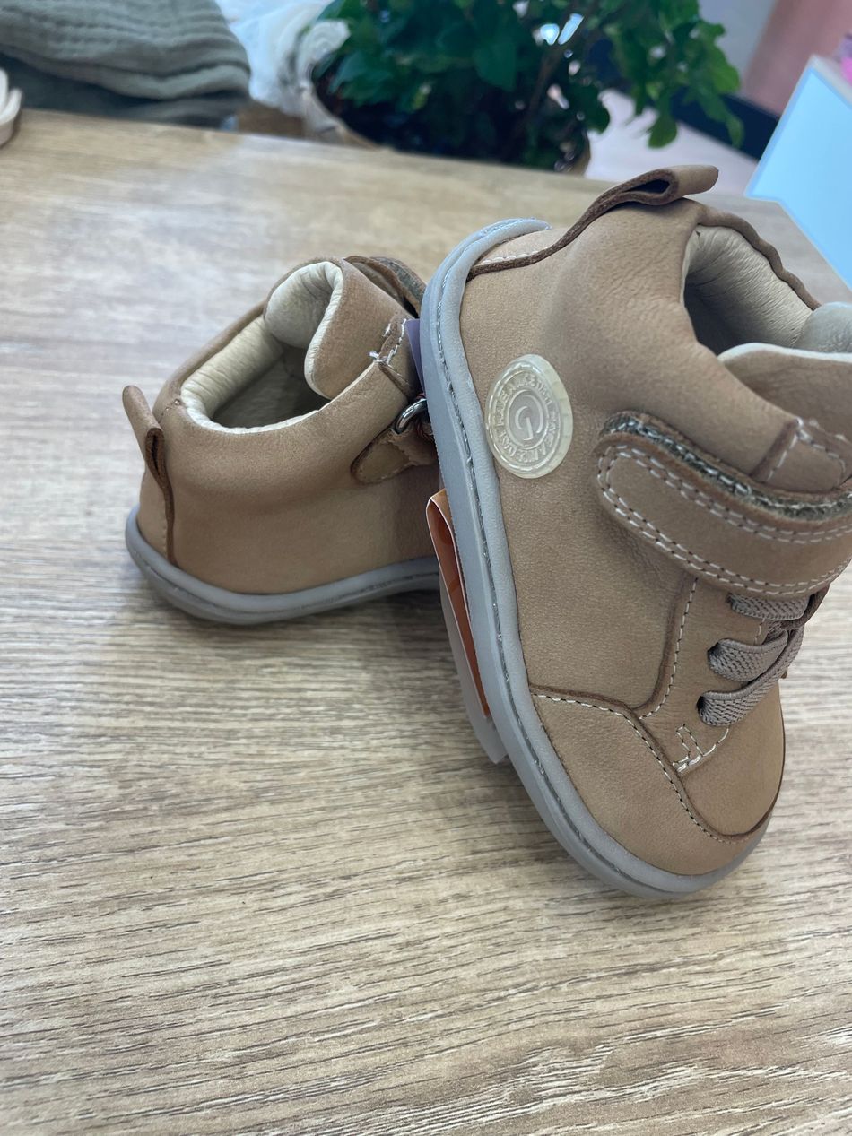 Scarpine beige chiaro da neonato con bordi grigi su un tavolo di legno, una appoggiata all’altra
