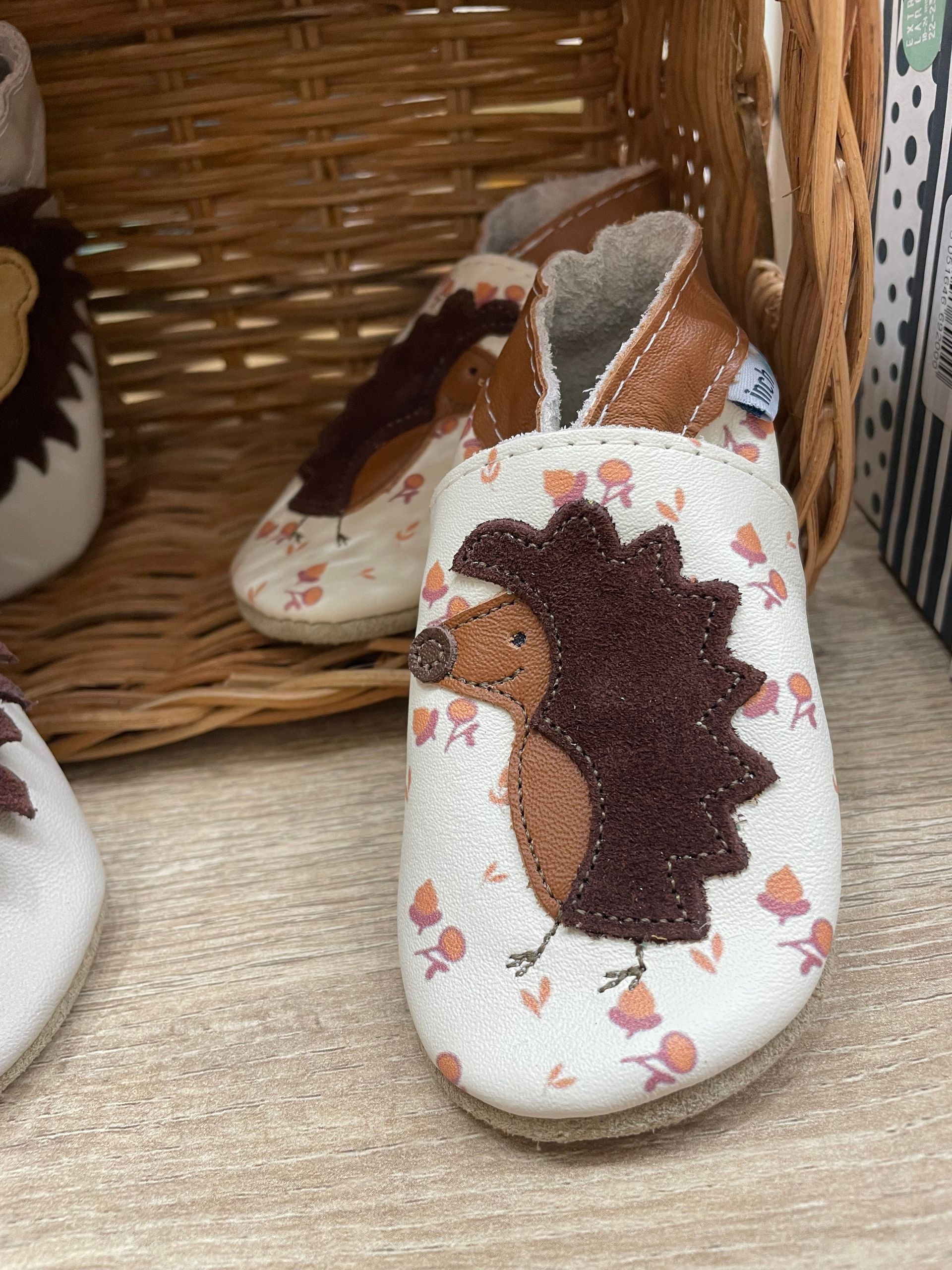 Scarpe slip-on bianche a fiori con tomaia marrone stringata, su una mensola di vimini
