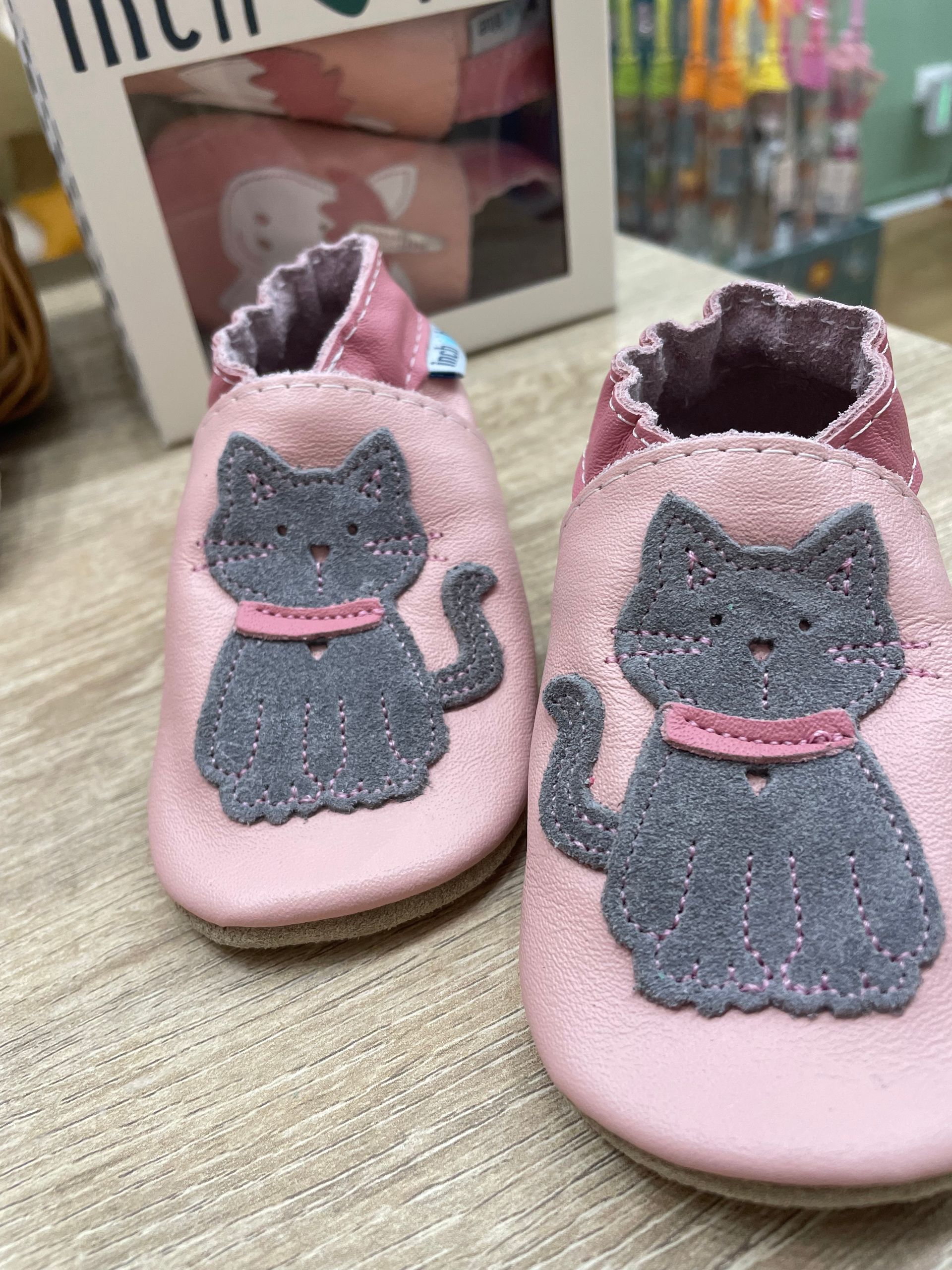 Pantofole rosa per bambini a forma di gatto, con gatti grigi scintillanti, su un tavolo.