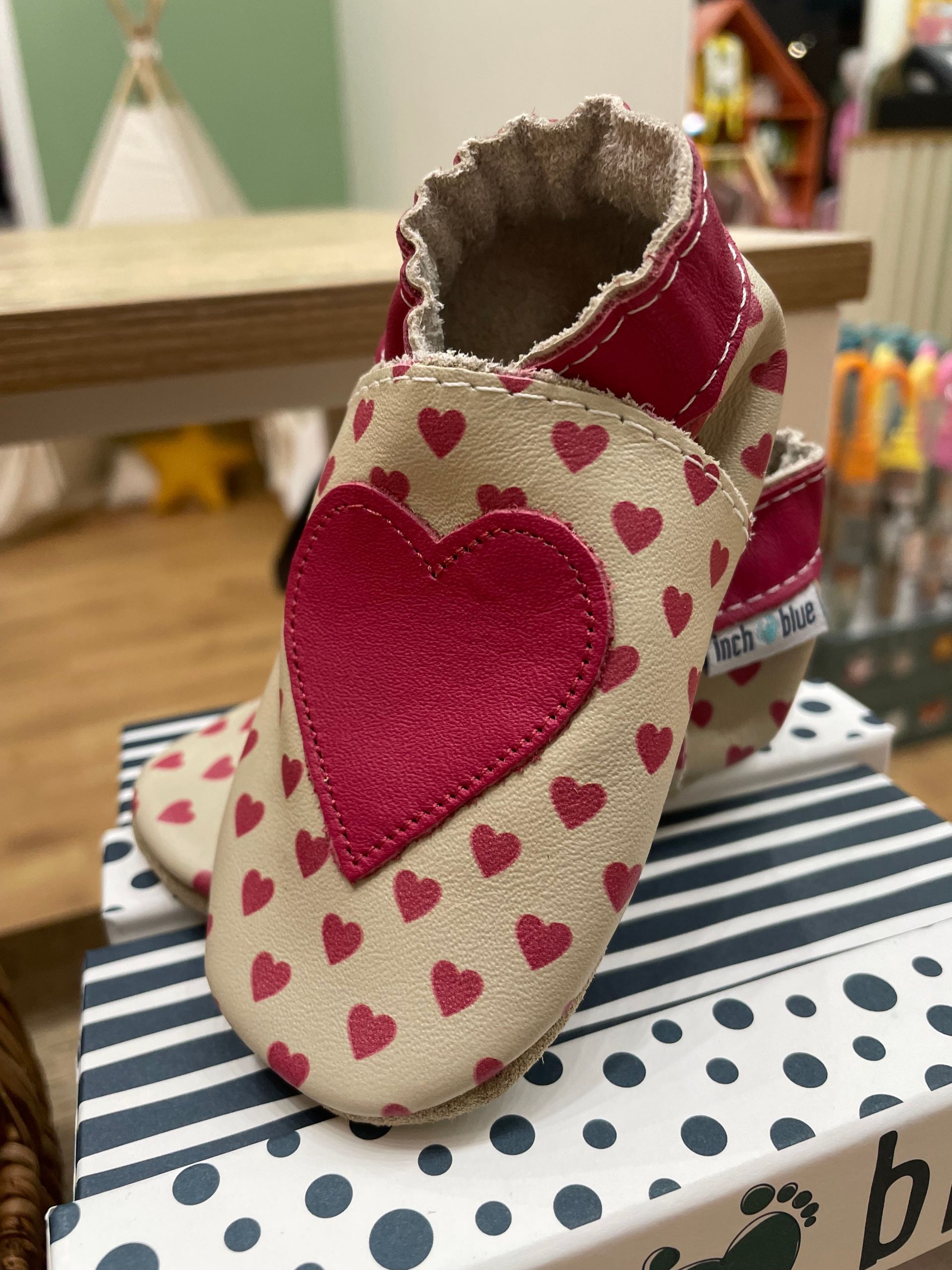 Paio di scarpine per neonati rosa e color crema con cuoricini, appoggiate su una scatola a pois