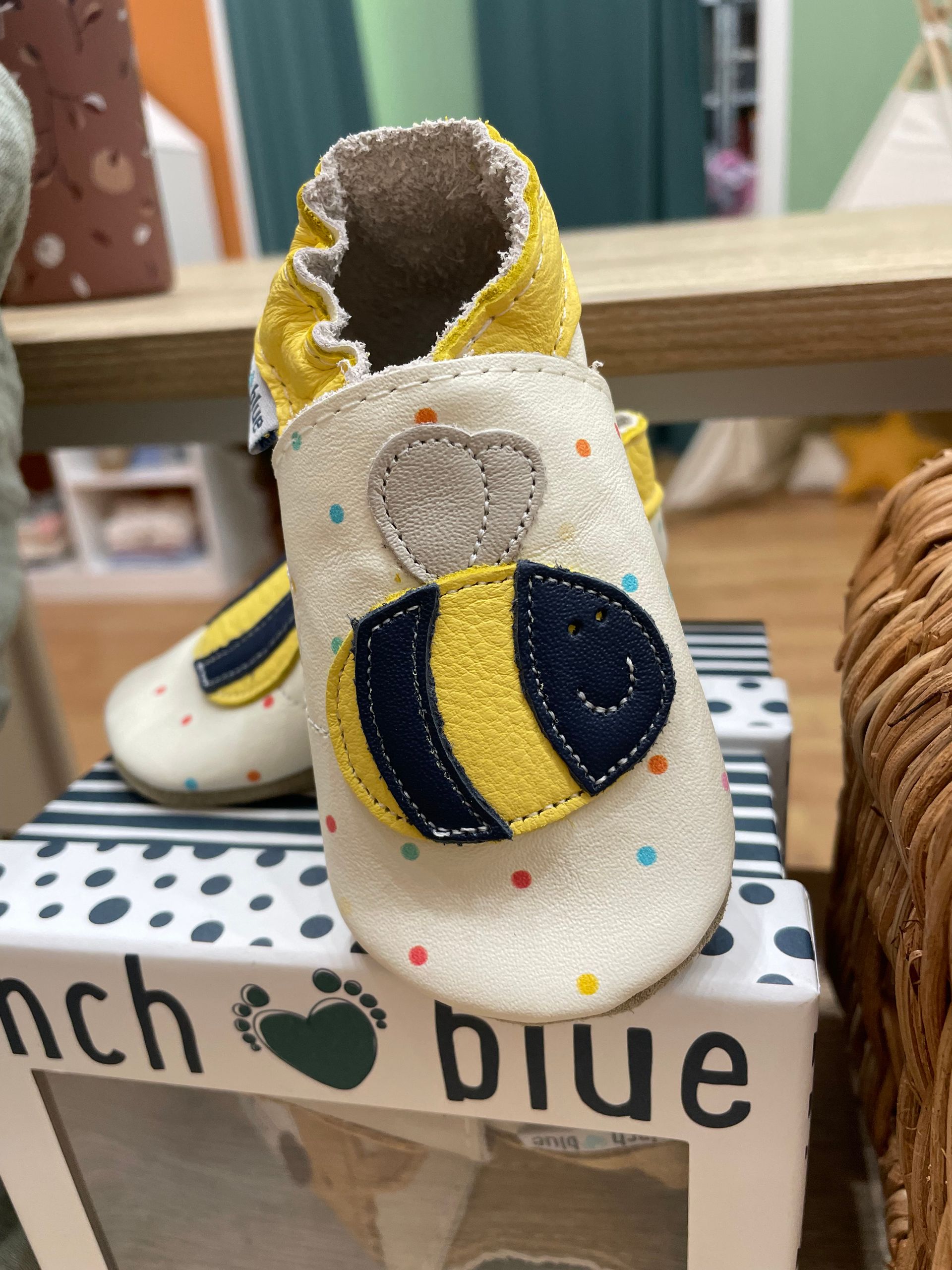 Scarpine decorative bianche da neonato con dettagli blu navy e gialli su uno scaffale
