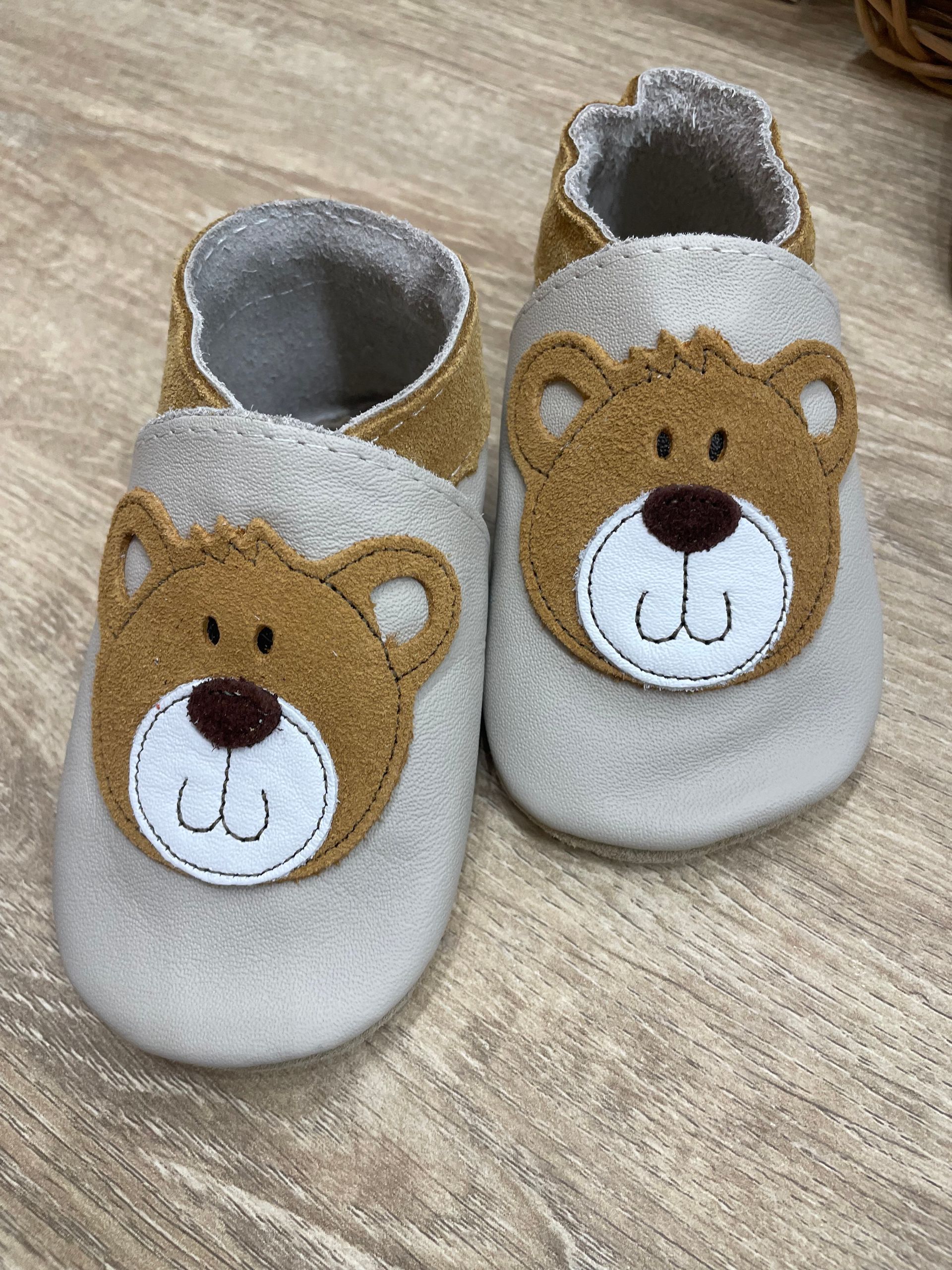 Paio di scarpine grigie per neonati con musetti d’orso su una superficie di legno.