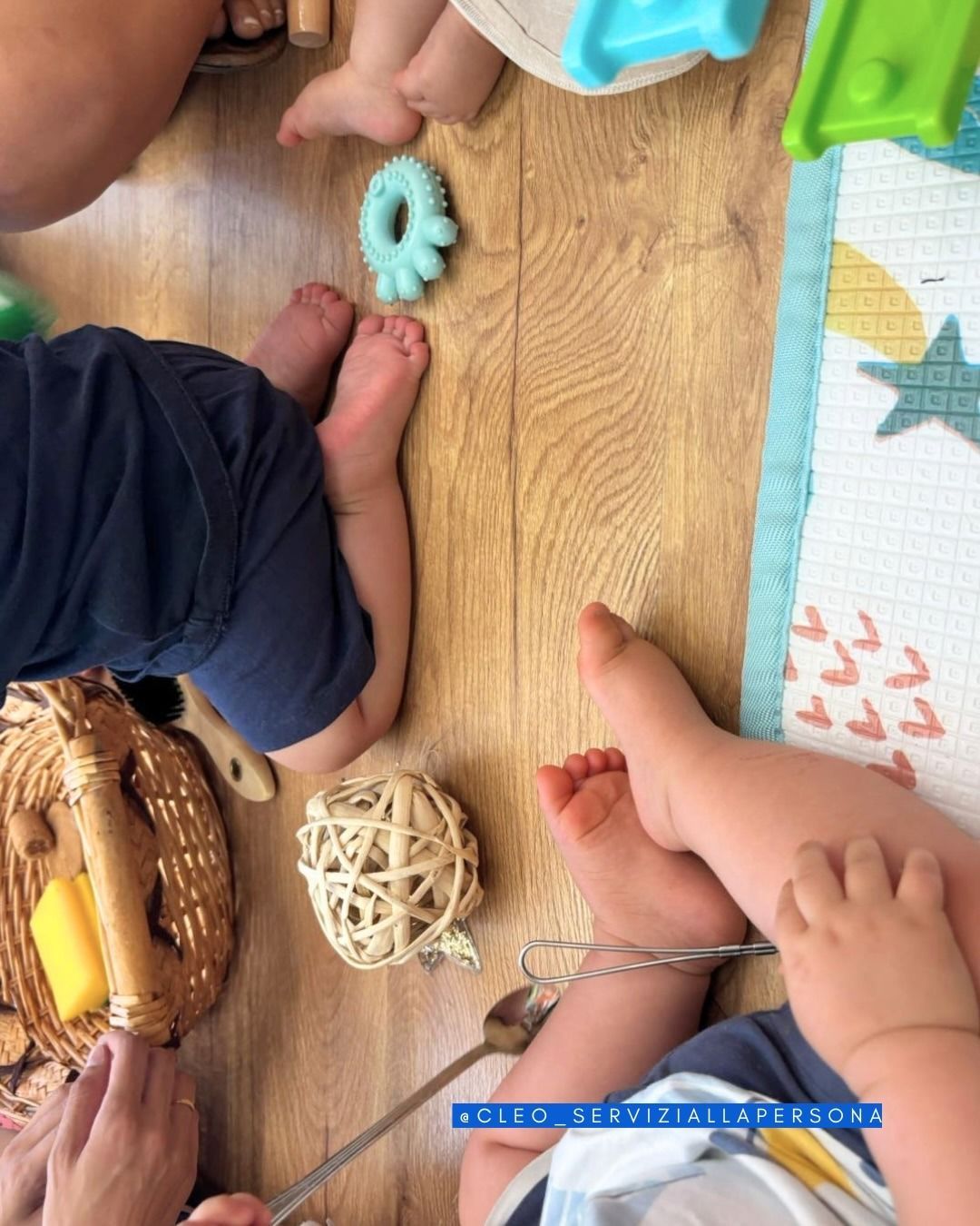 Mani e piedi di un bambino piccolo su un tappetino da gioco in legno, con peluche e un cestino di vimini lì vicino