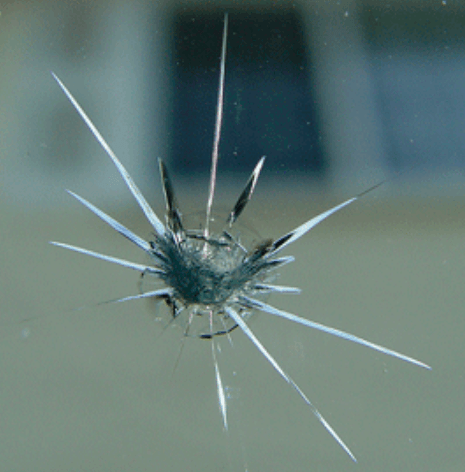 Spiderweb crack on a glass window, radiating outward from a central point.