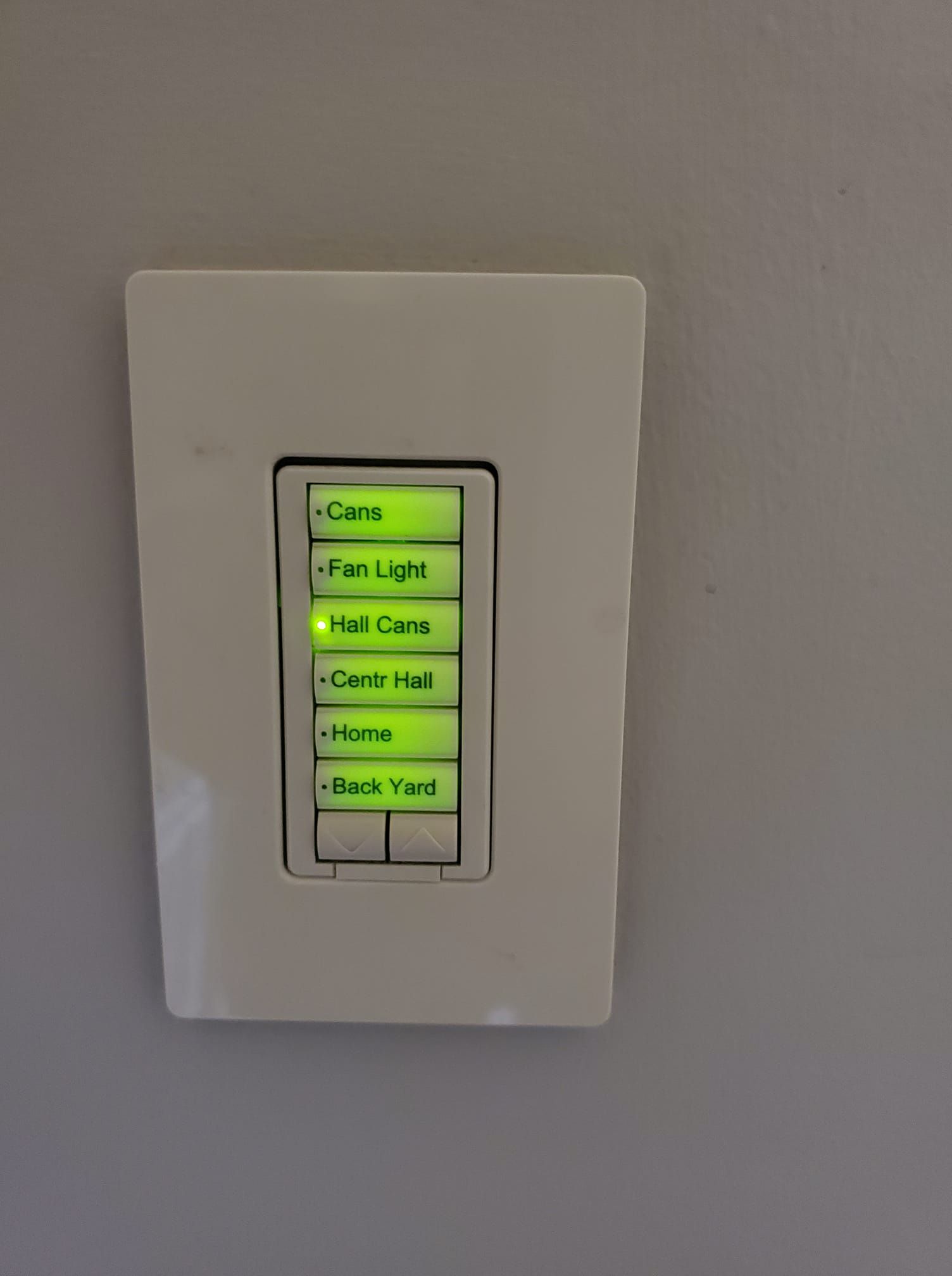 A white light switch with green buttons on a white wall.