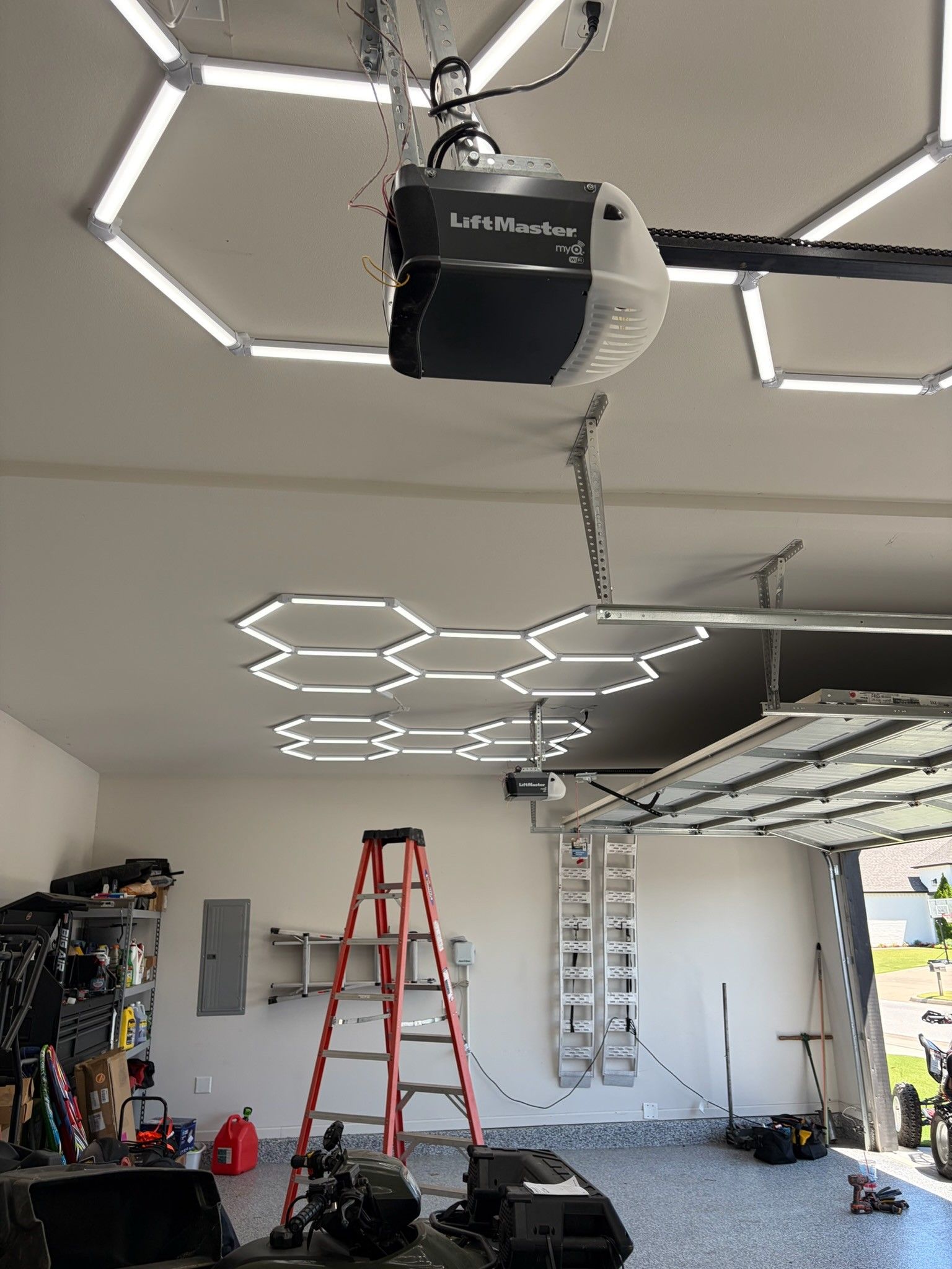 Garage with ceiling LED lights, open garage door, ladder, tools, and a garage door opener overhead.