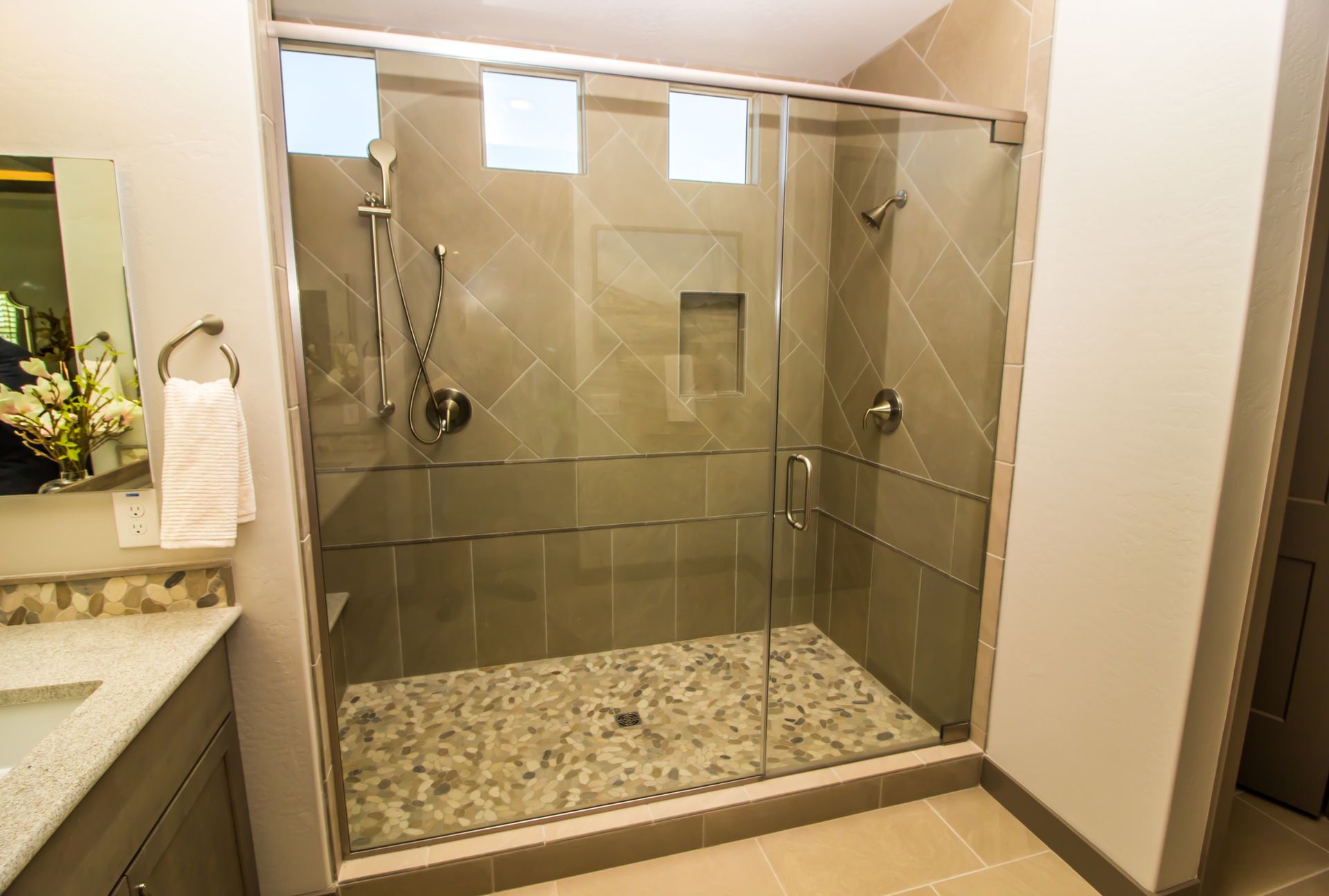 Modern shower with clear glass doors and pebble floor. Beige tile walls and chrome shower fixtures.
