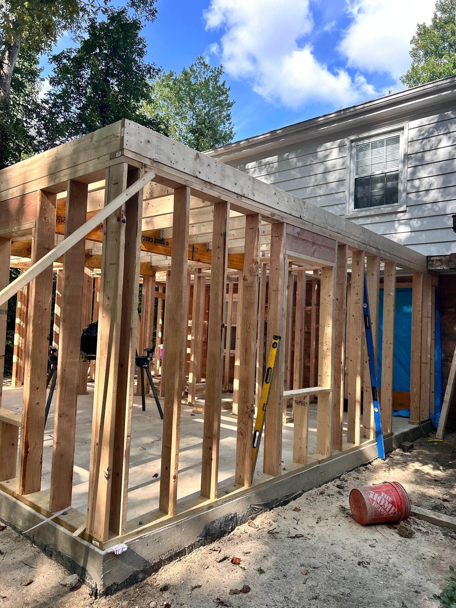 Wooden framing of a building addition under construction attached to a house, on a concrete foundation.