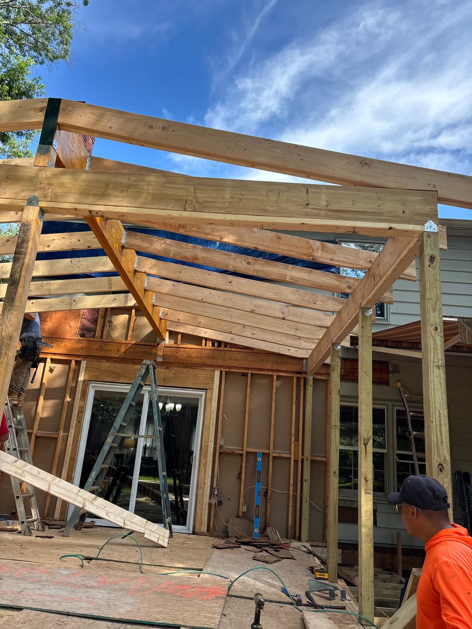 Construction of a wooden pergola or patio cover next to a house, involving exposed beams.