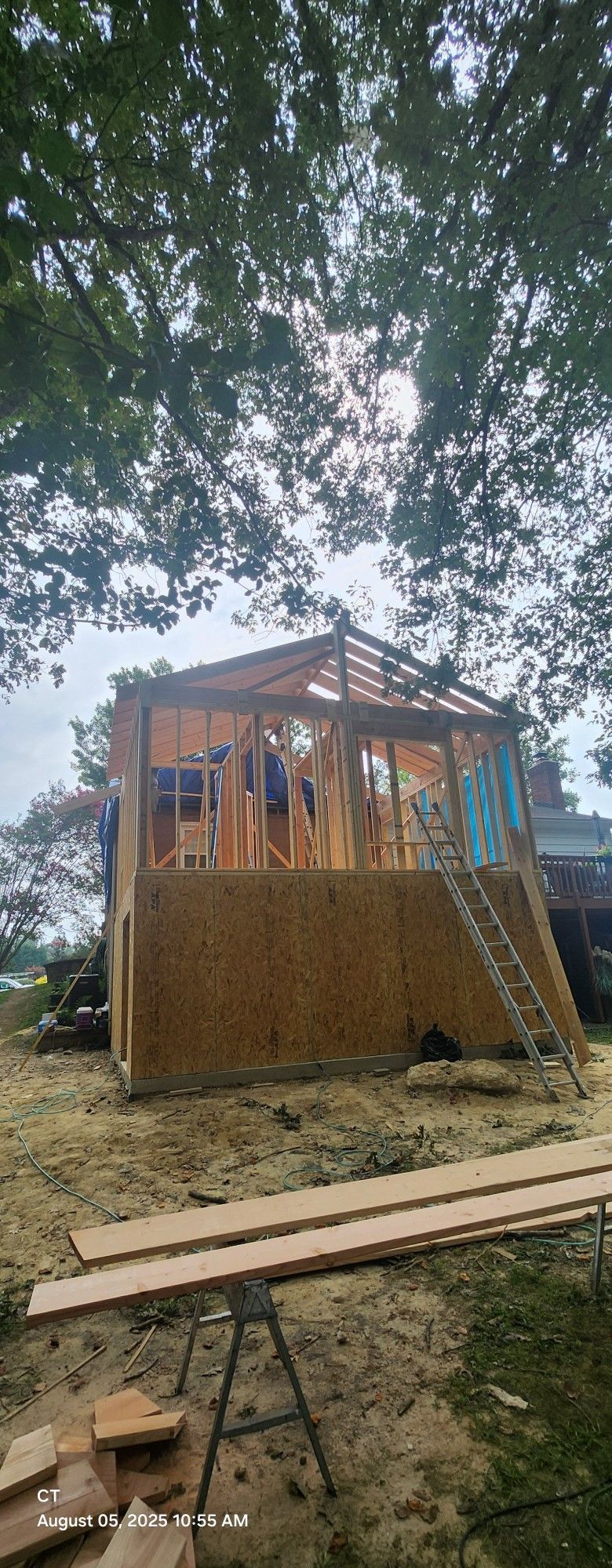 A partially constructed wooden building under a bright sky, with a ladder leading up the side.