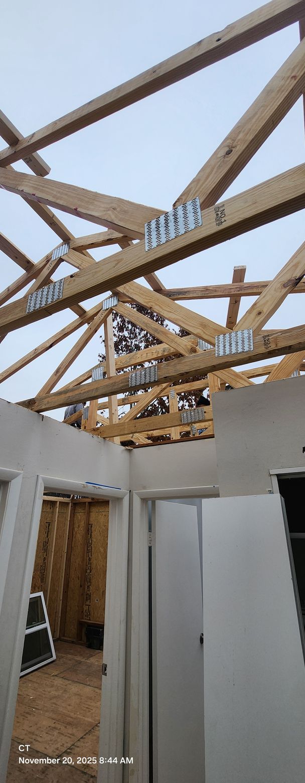 Interior view of a building under construction. Wooden roof frame above white walls with doorways.
