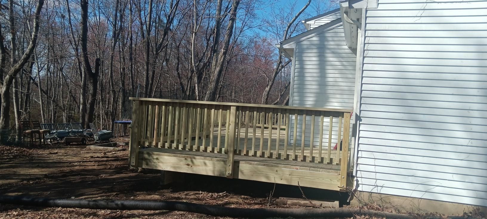 Wooden deck attached to a white house, surrounded by trees.