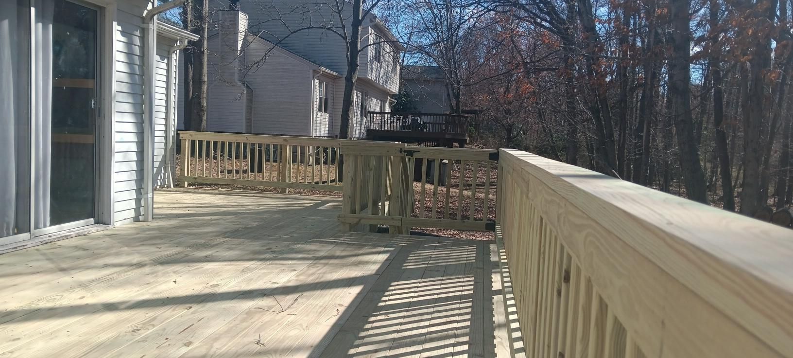 Wooden deck with railing overlooking a wooded area and other houses.
