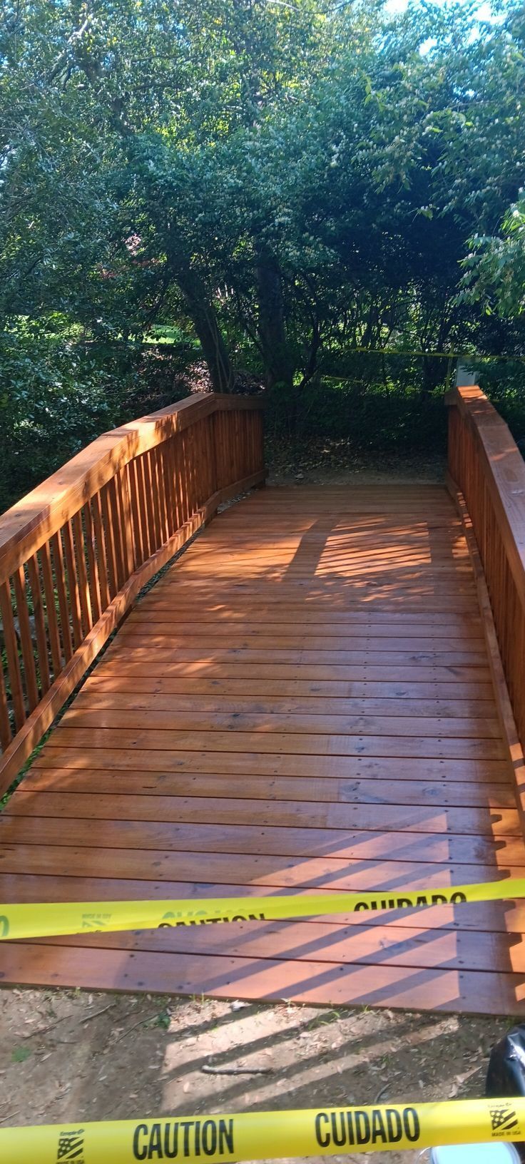Wooden bridge with caution tape, leading into a shaded forest.