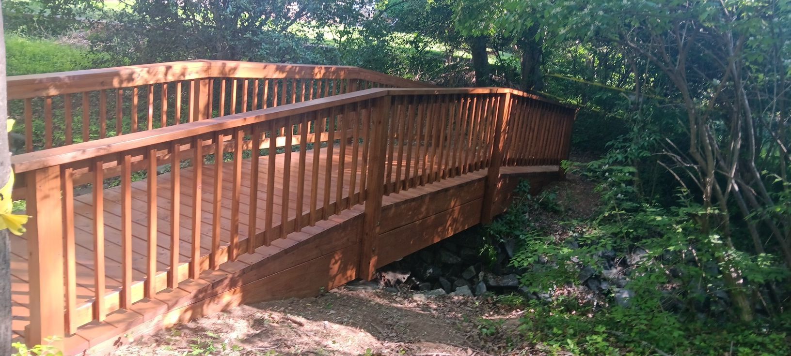 Wooden bridge over a rocky area, surrounded by lush green trees and foliage.