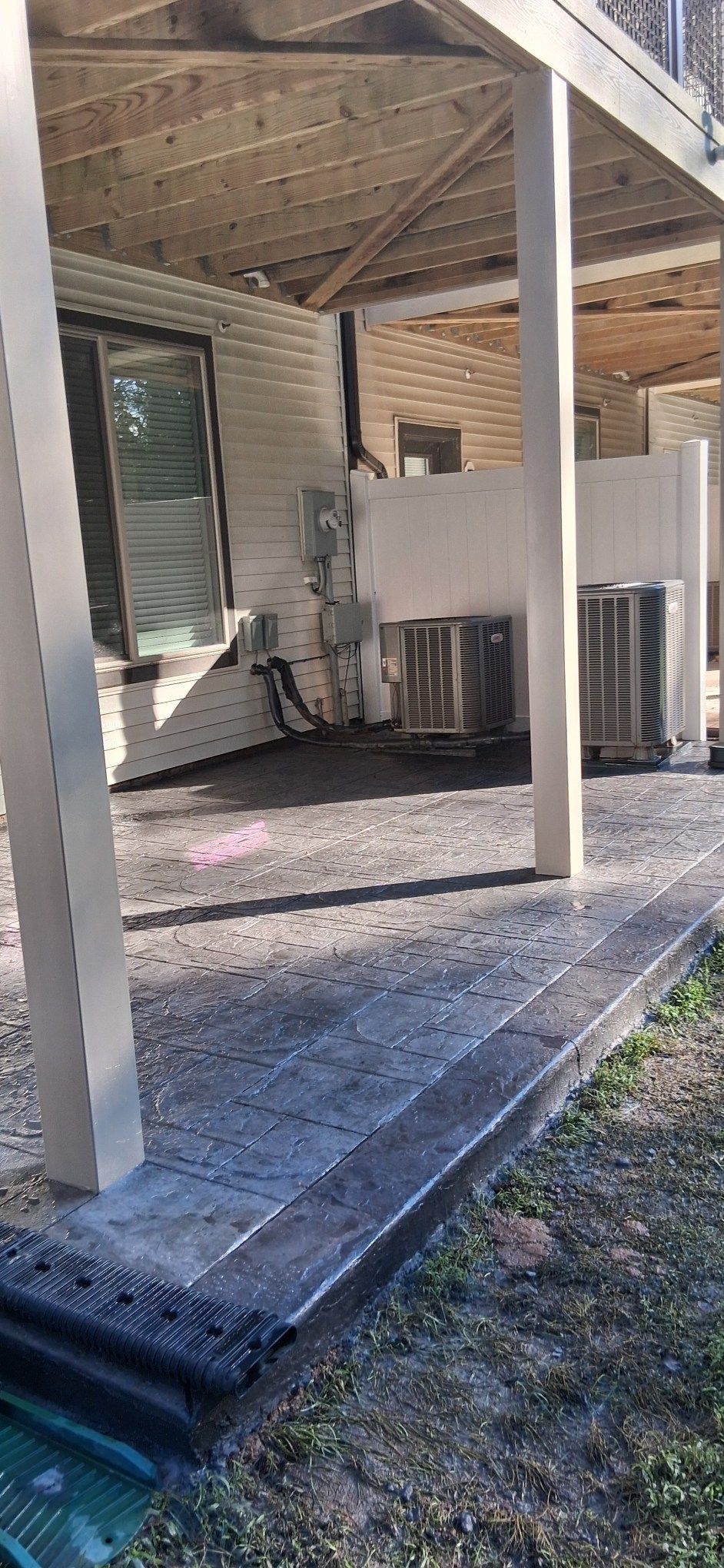 A concrete patio under a deck, with an AC unit and utility box visible.