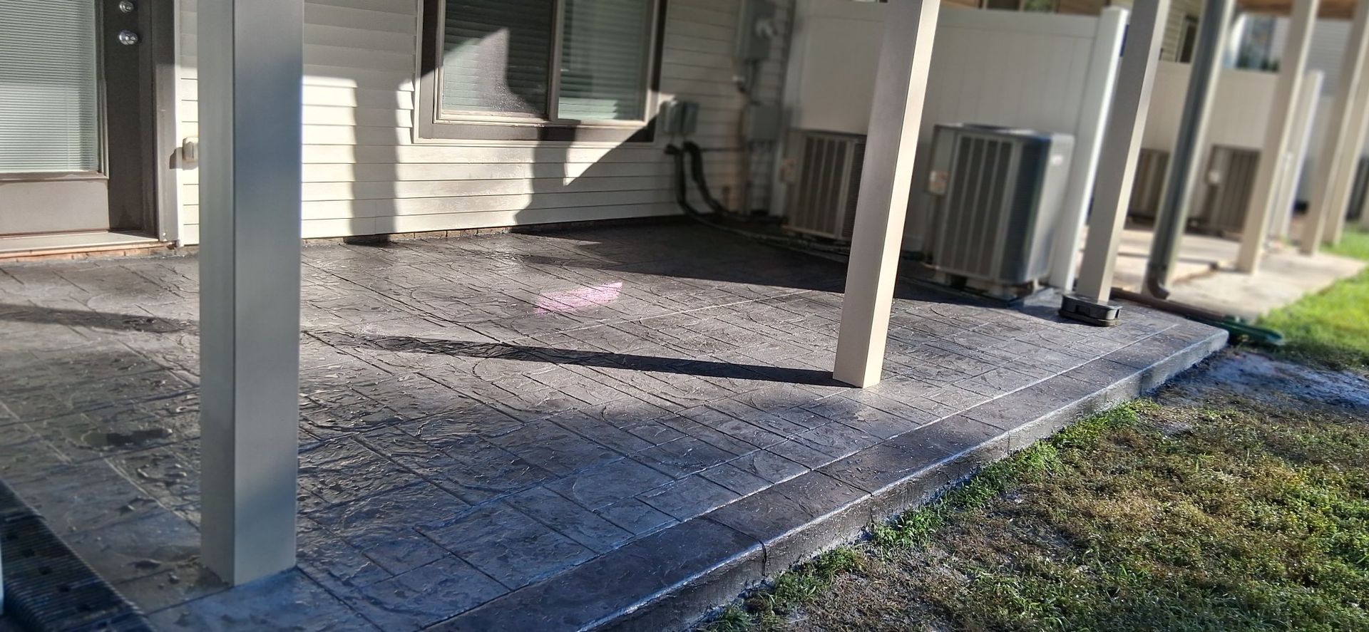Gray concrete patio with support beams, grass, and an air conditioning unit.