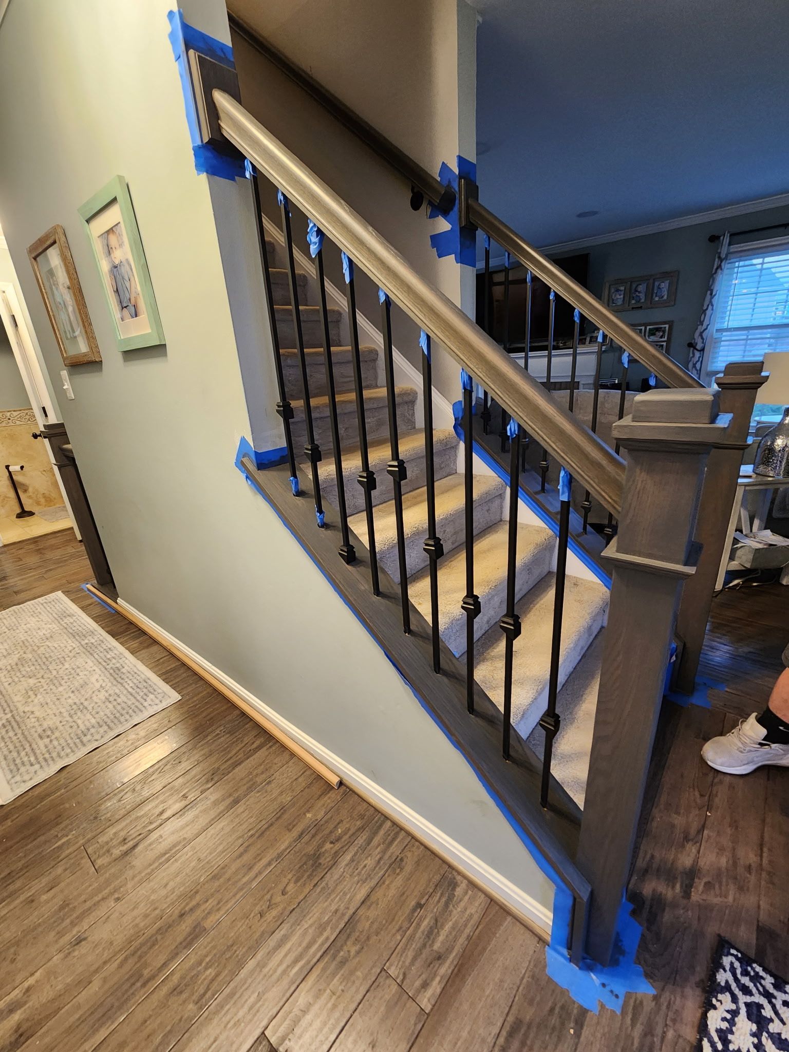 Staircase with gray balusters, black iron spindles, and wood handrail. Walls are blue-gray, with painter's tape in place.