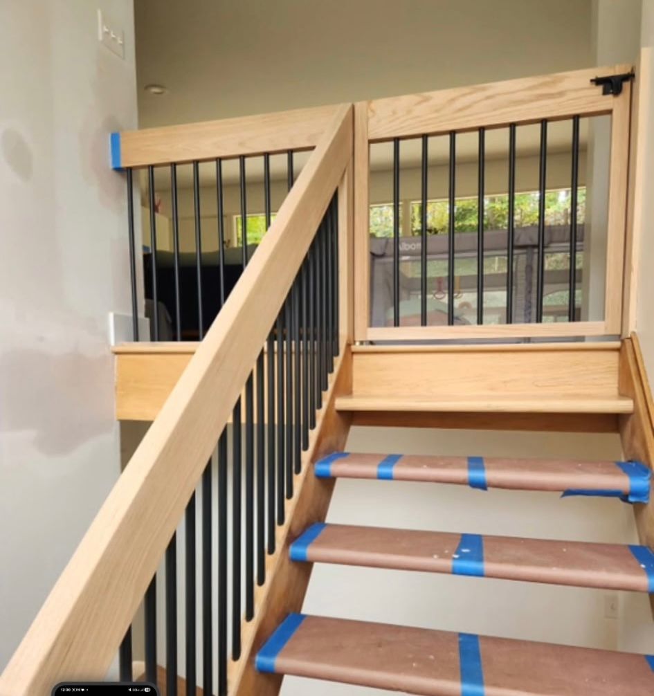 Staircase with wooden railing, black spindles, and a baby gate at the top.