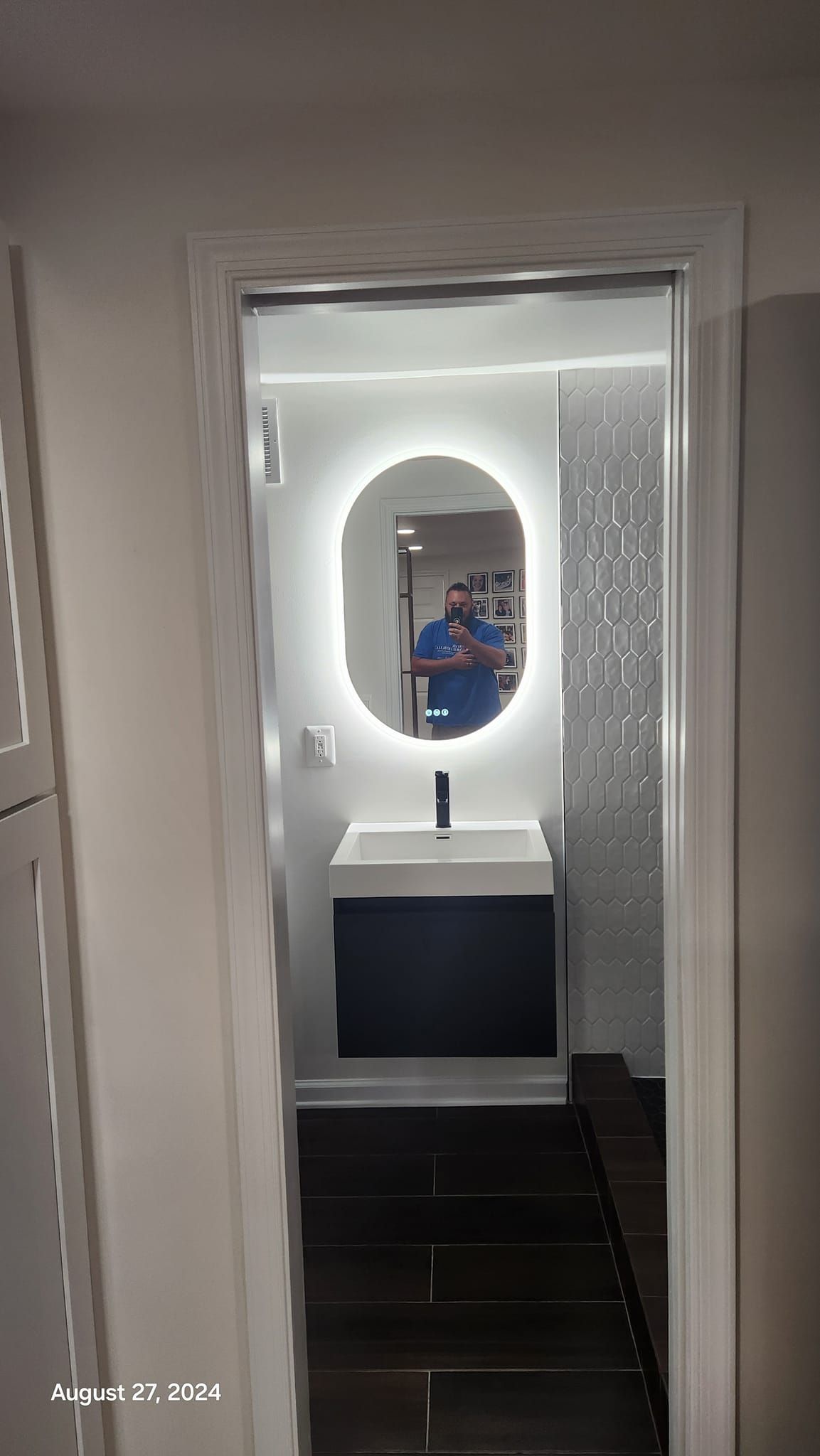 Bathroom with oval mirror, sink, dark cabinet, and white tiled wall.