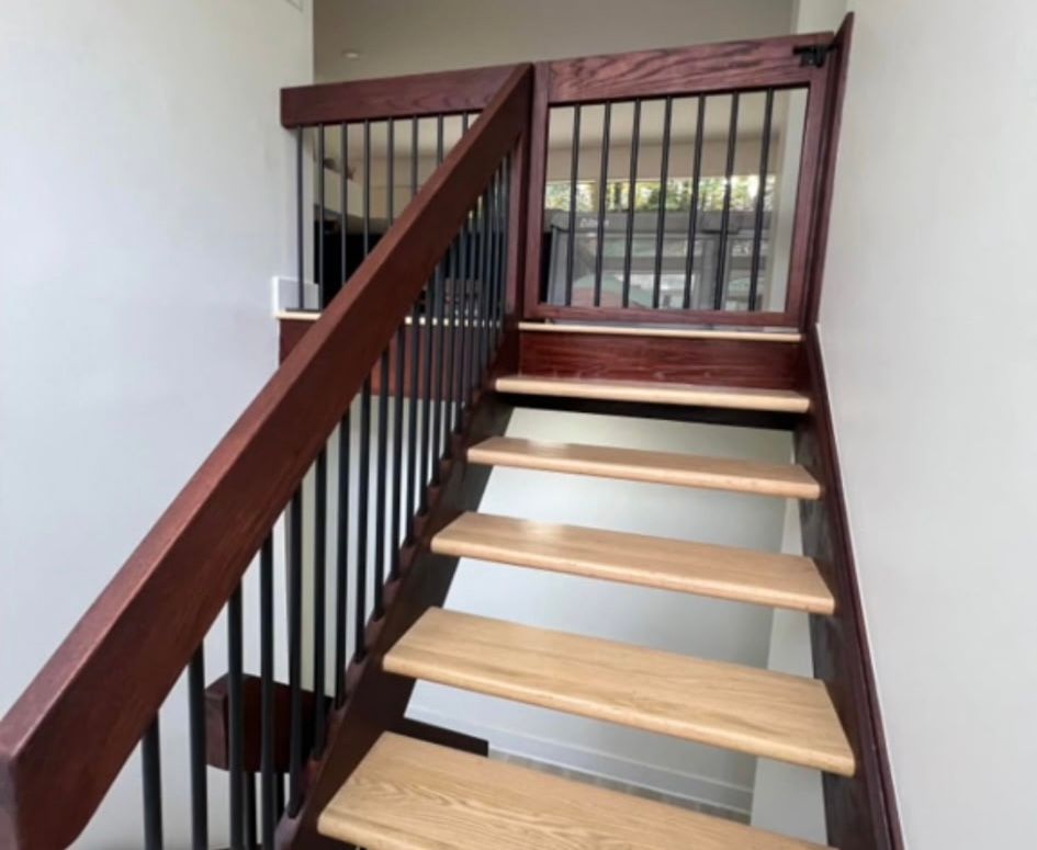 Wooden staircase with gate at the top. Dark brown banister and black metal spindles.  Wooden stairs with blonde treads.