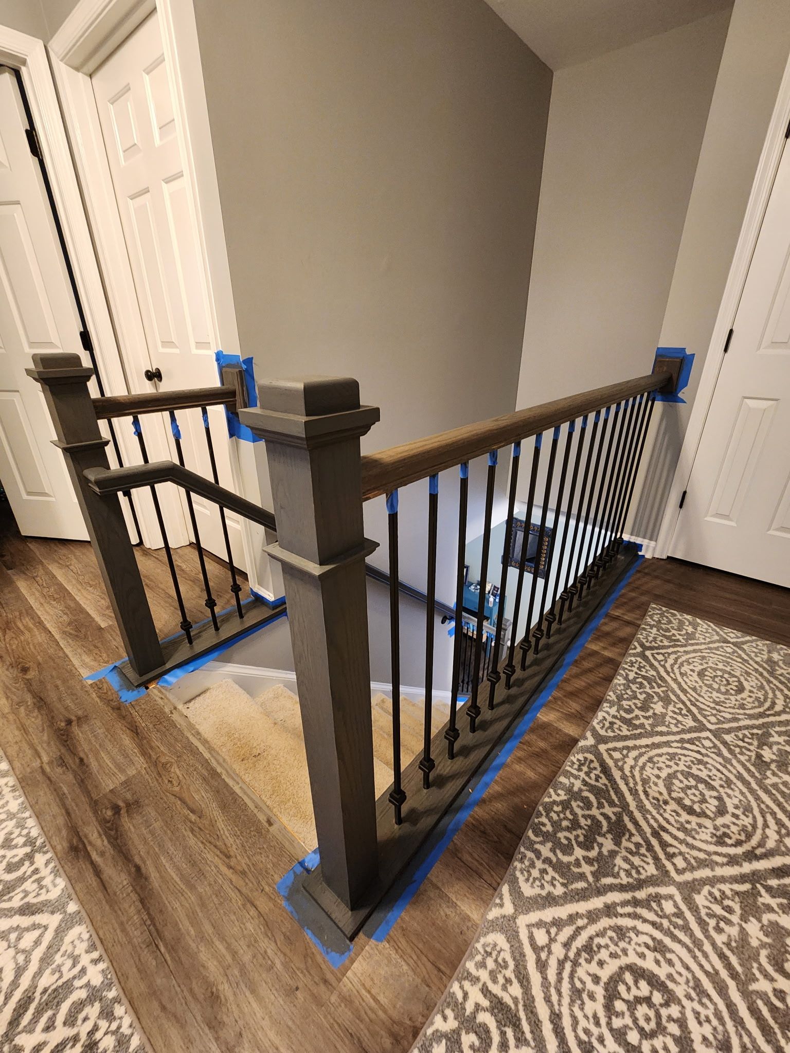 Staircase with gray balusters, black spindles, wood handrail, and beige and brown patterned carpet.