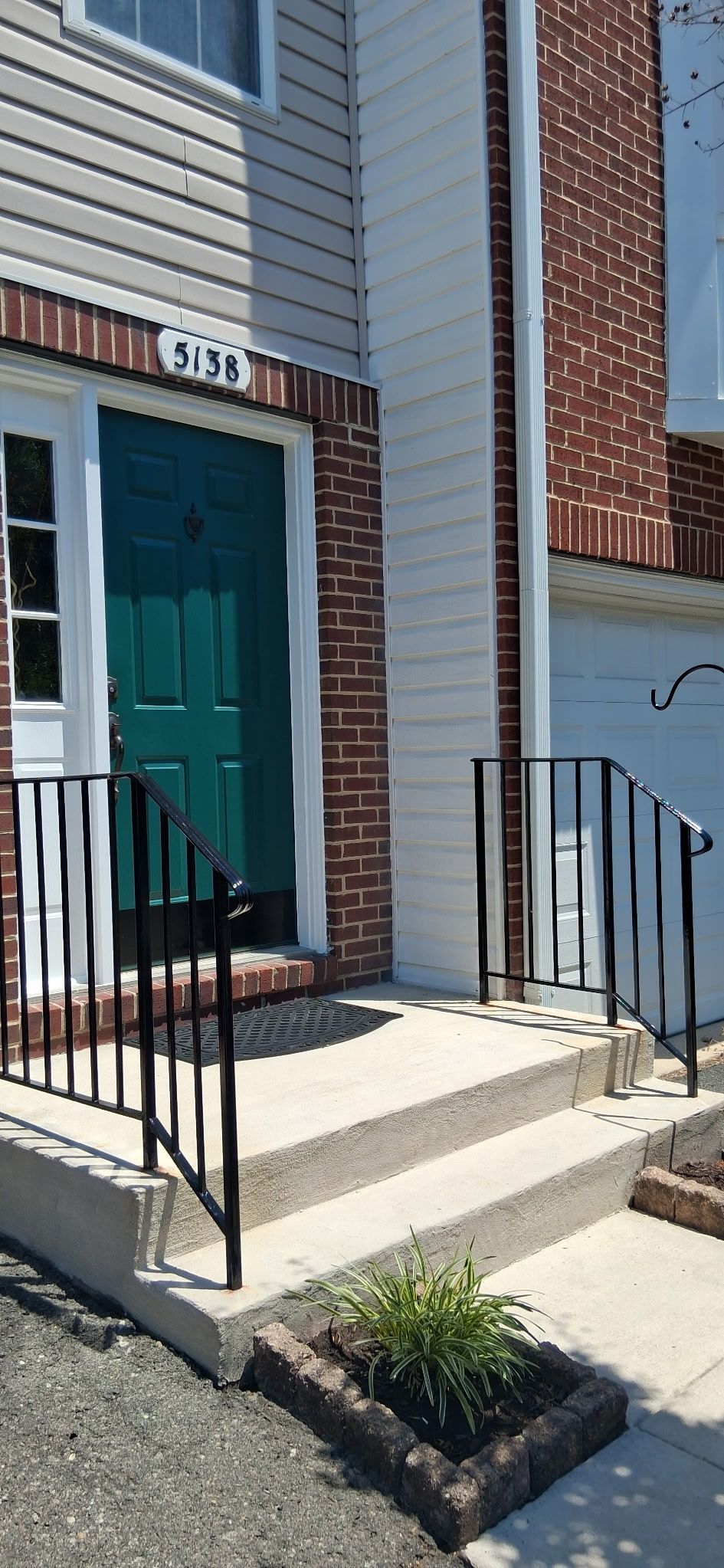 Front entrance of a townhouse with teal door, white siding, and black metal railings by concrete steps