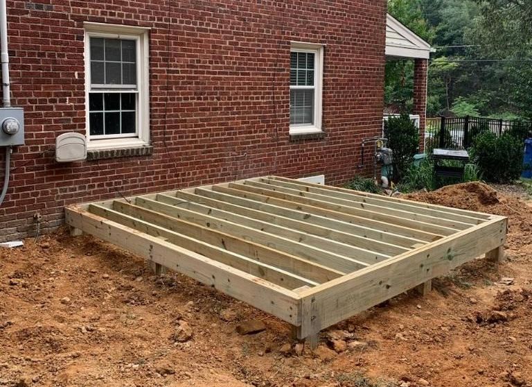 A wooden deck is being built in front of a brick house.