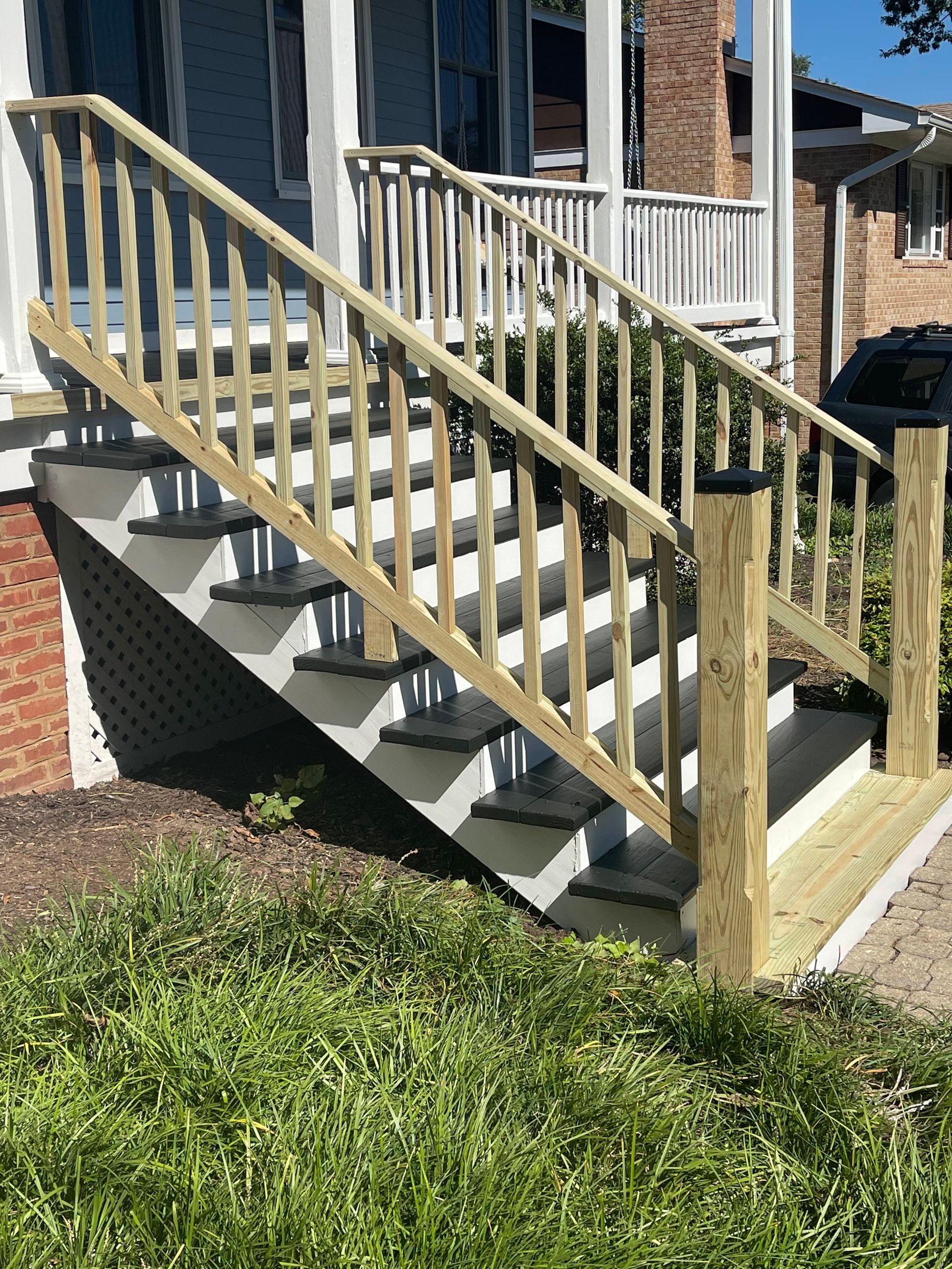 Exterior wooden staircase with beige railings beside a brick house and grass yard