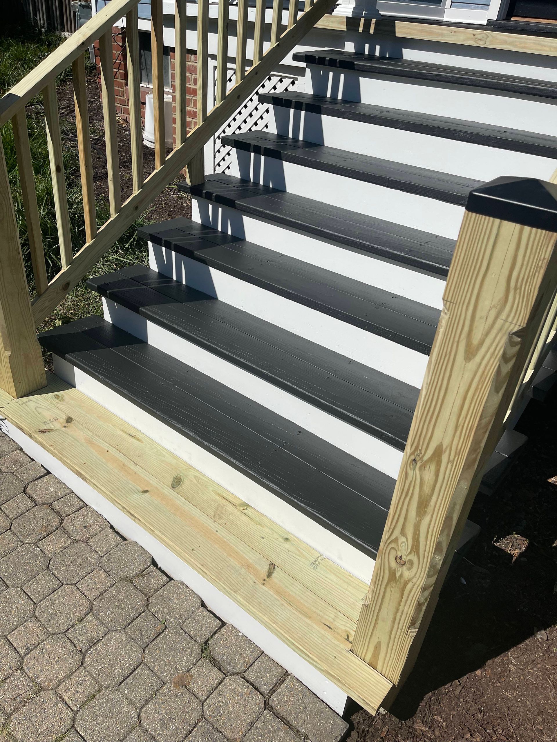 Wooden outdoor staircase with dark gray steps and railings on a brick-paved path.