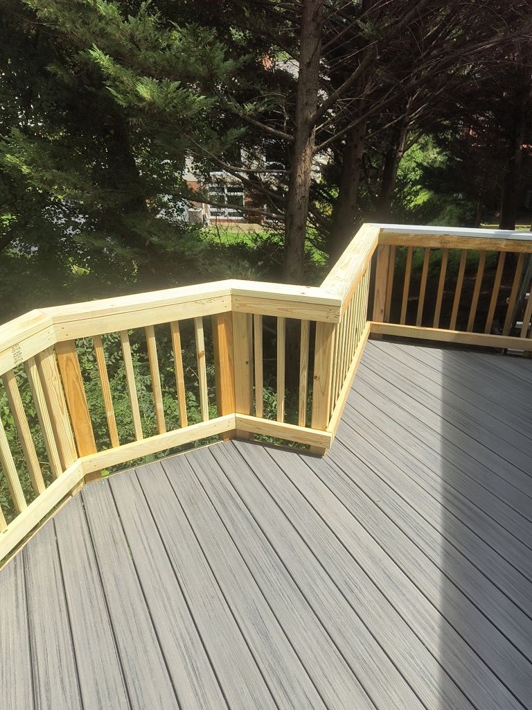 Wooden deck with gray planks and pale railings overlooking a leafy backyard.