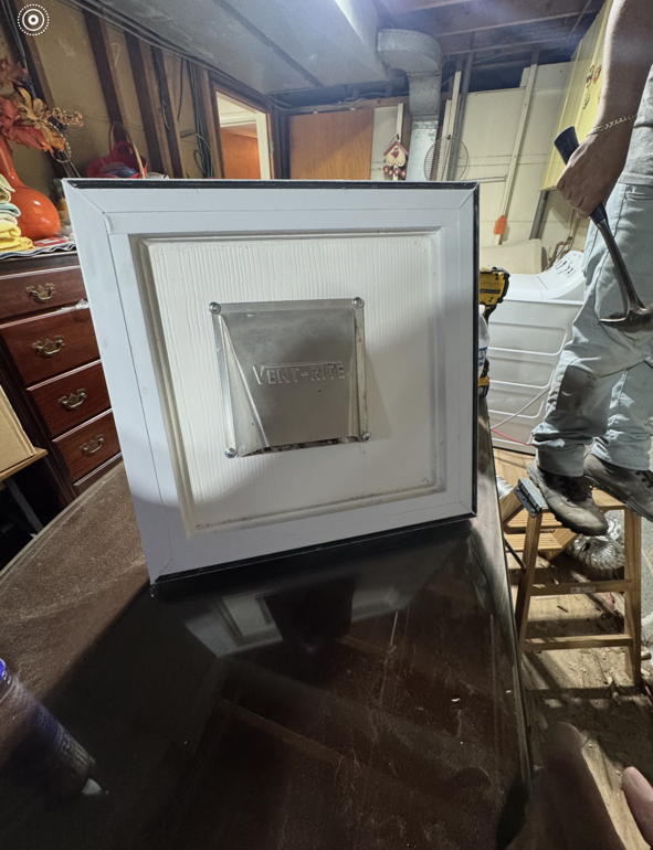 A white-framed ventilation cover is installed on a wall, likely in a basement or utility space.