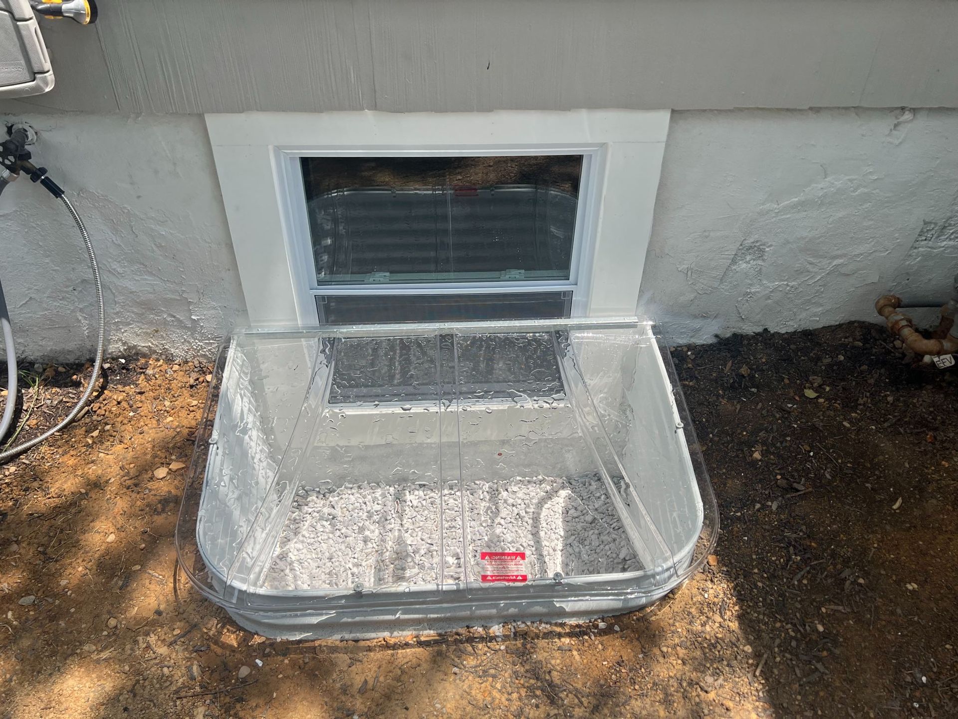 Clear plastic pet door cover propped against a small basement window in a stucco wall.