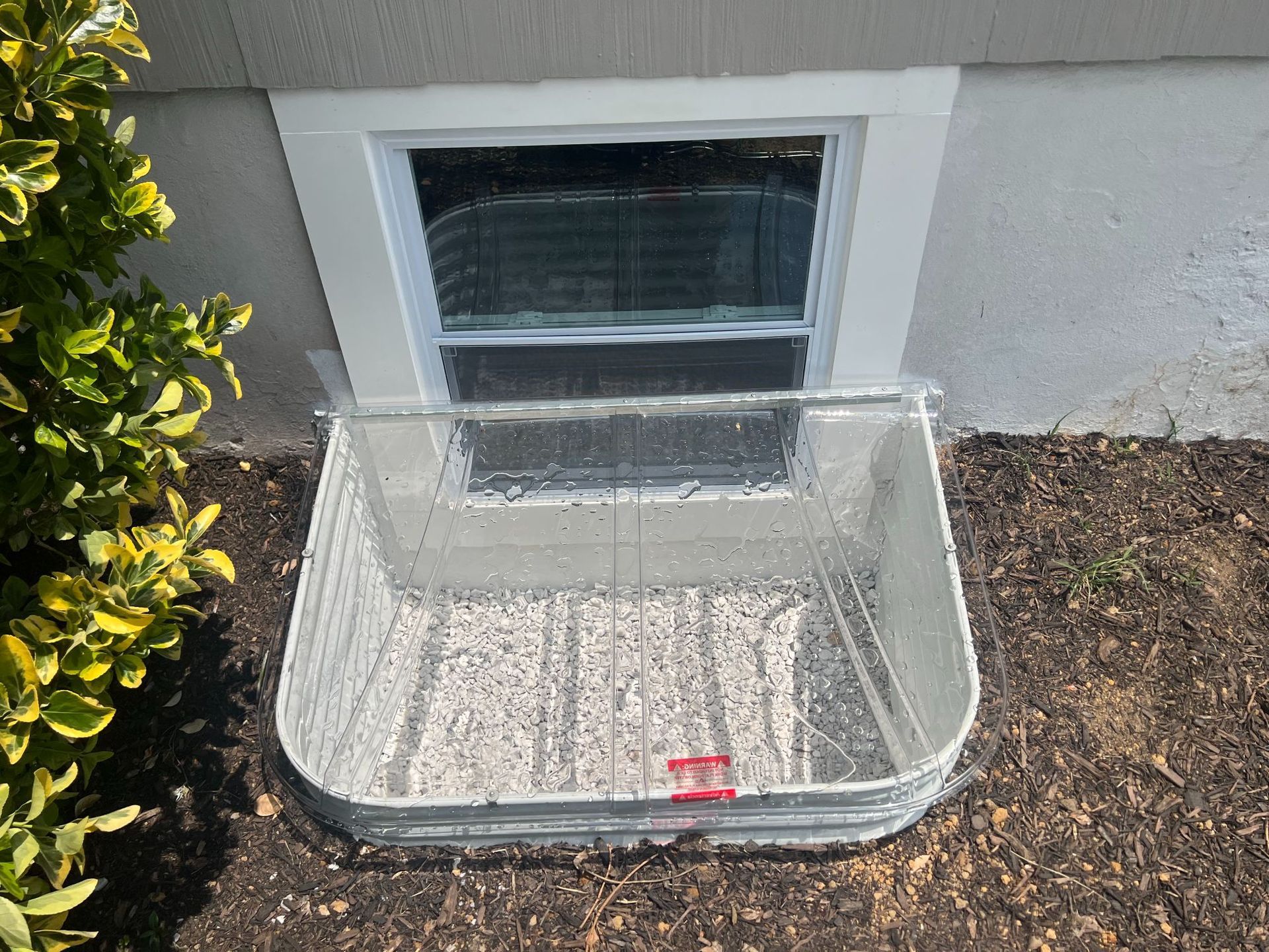 Metal pet crate beside a house window against a stucco wall