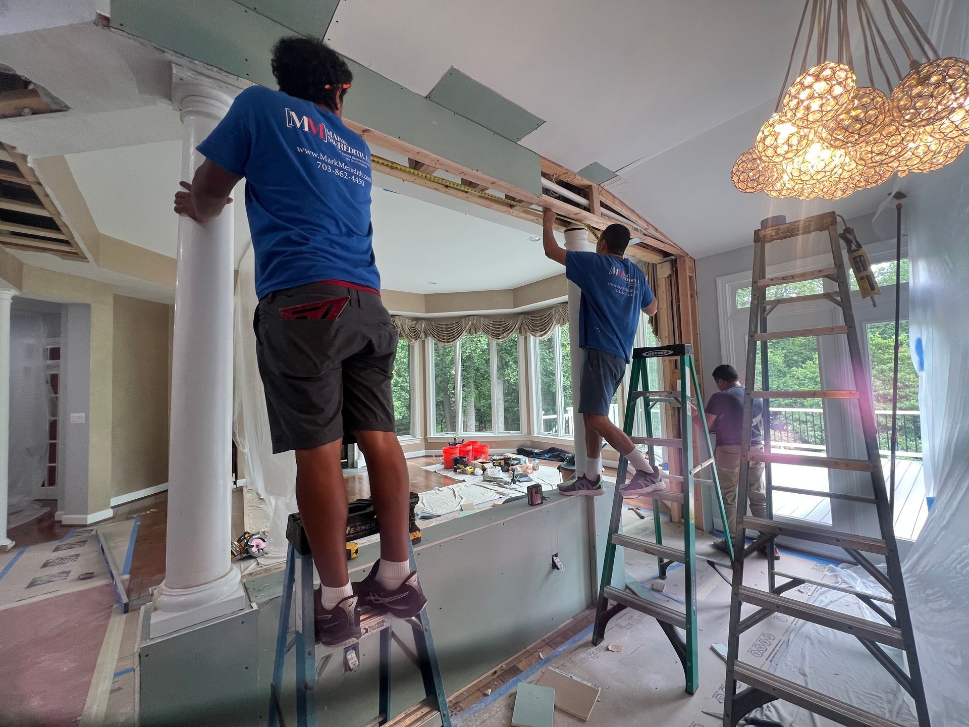 People on ladders installing a ceiling fixture in a bright room under renovation